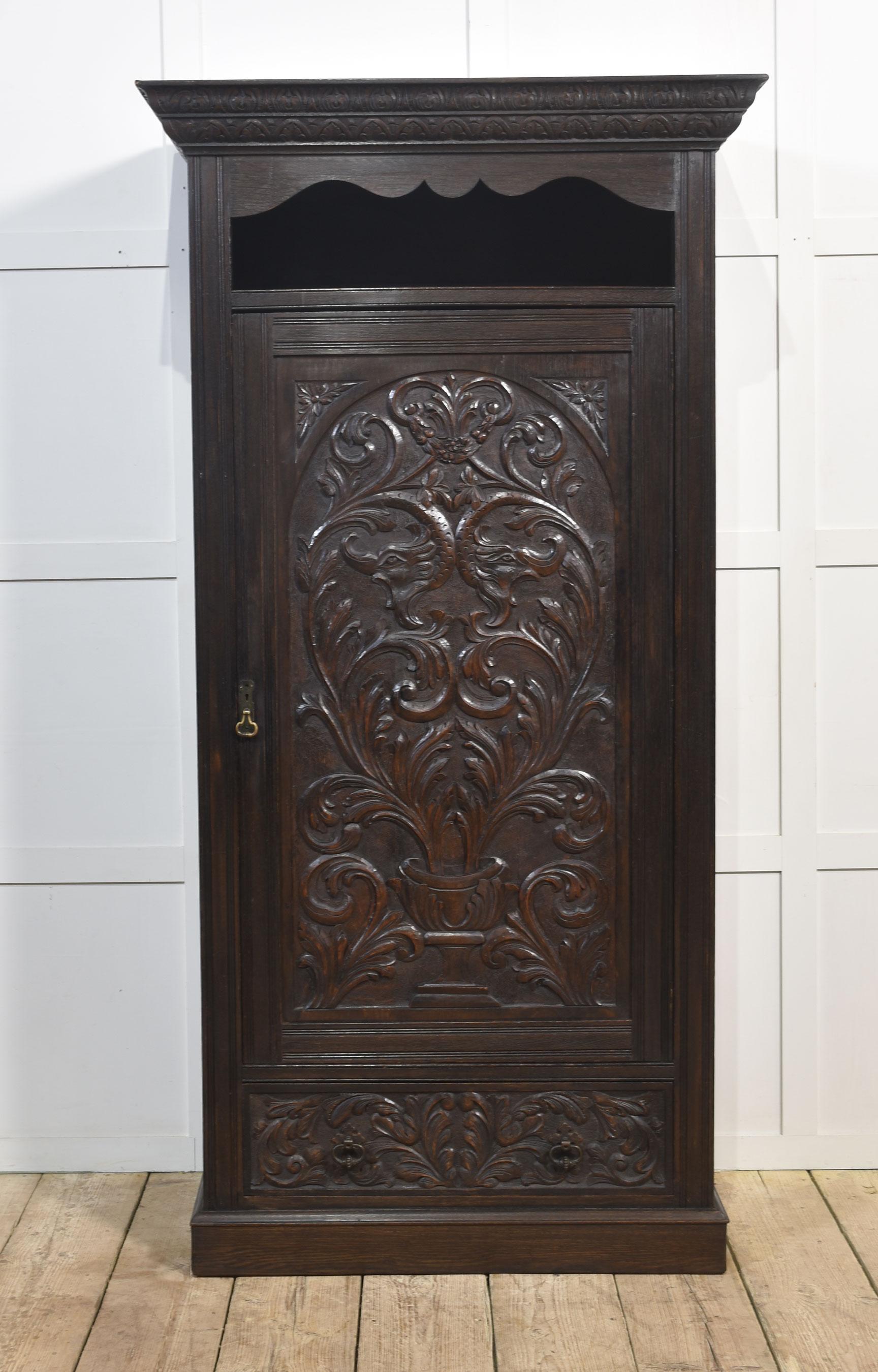 Solid oak hall robe, the moulded cornice above open cupboard to the door having urn and scrolling relief and central dolphin decoration. opening to reveal hanging area. The base is fitted with a long drawer. All raised up on a plinth