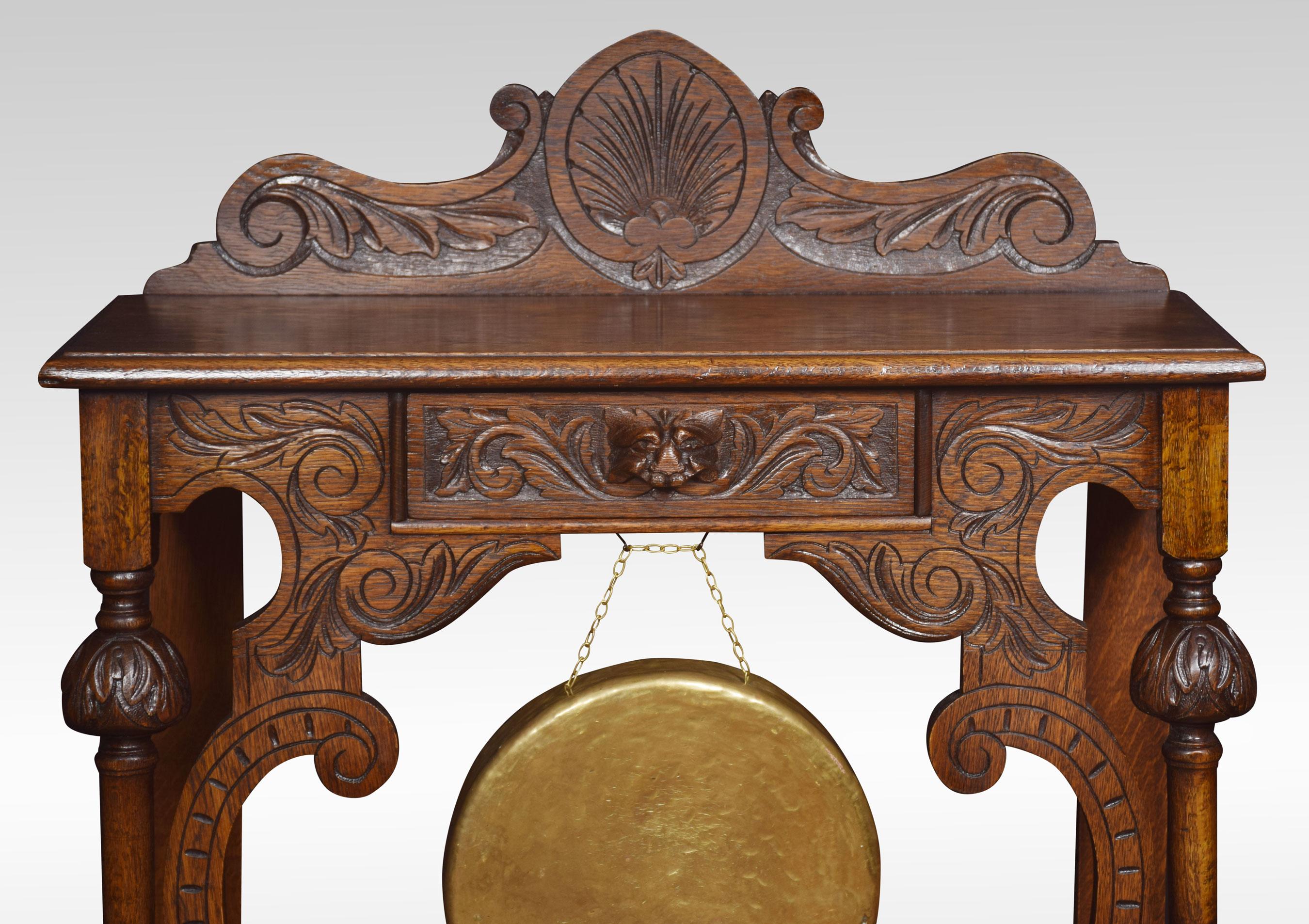 Carved oak hall table, the top of rectangular form with raised gallery above a carved central drawer with mask handle and brass gong below. Raised up on turned supports united by under tier. All raised up on bun feet.
Dimensions:
Height 41