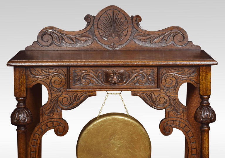 Carved oak hall table, the top of rectangular form with raised gallery above a carved central drawer with mask handle and brass gong below. Raised up on turned supports united by under tier. All raised up on bun feet.
Dimensions:
Height 41