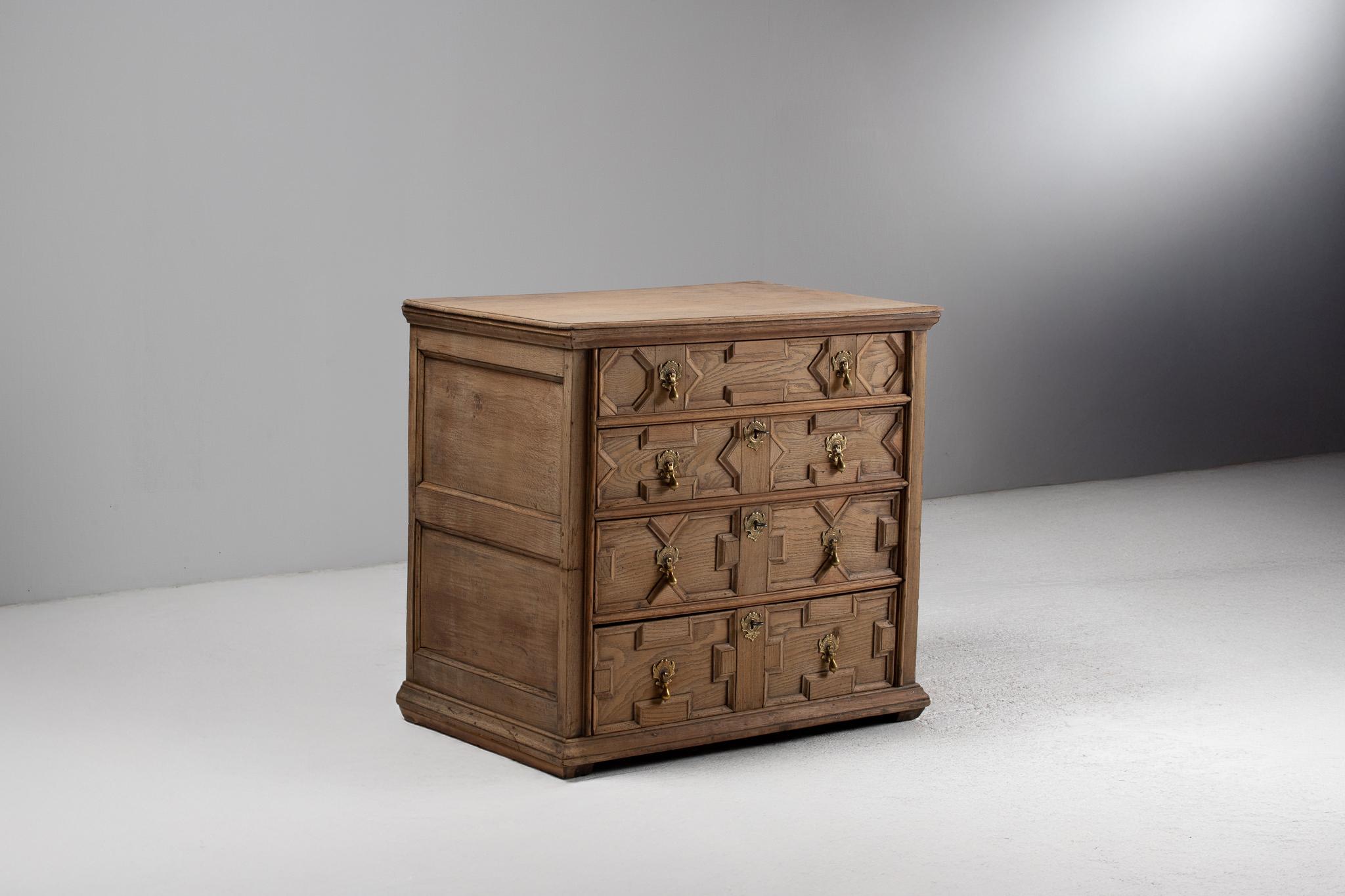 A reverent echo of 17th century English cabinetry, this 19th-century oak chest of drawers embodies the bold geometry and sculptural massing of the Jacobean tradition. The façade is animated with applied moldings—angular lozenges, chamfered
