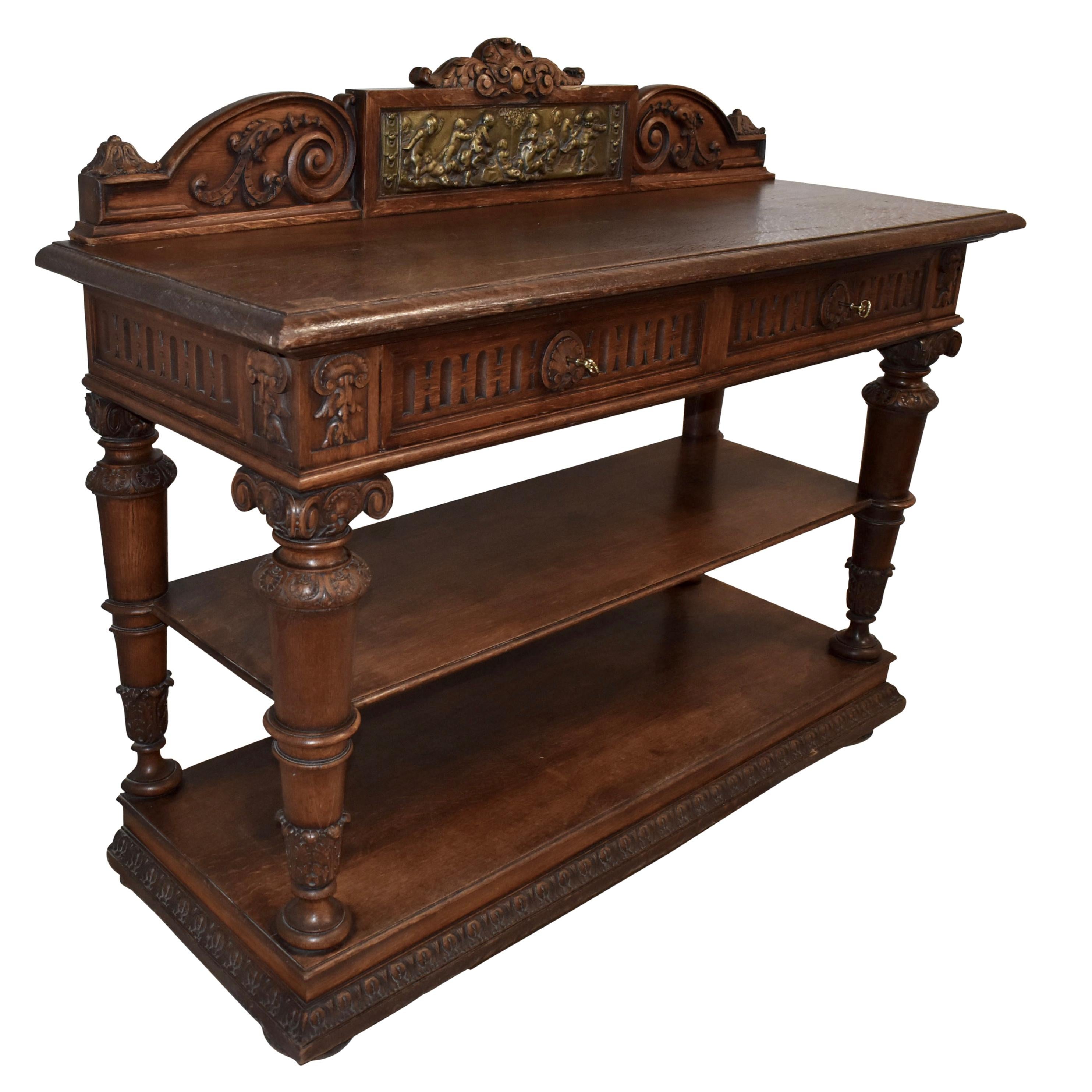 Made of oak and finished with a medium stain, this beautiful server from the beginning of the 20th-century is a feast for the eyes! From the elaborately carved crown over the backboard down to its crescent bun feet at the base, everything about the
