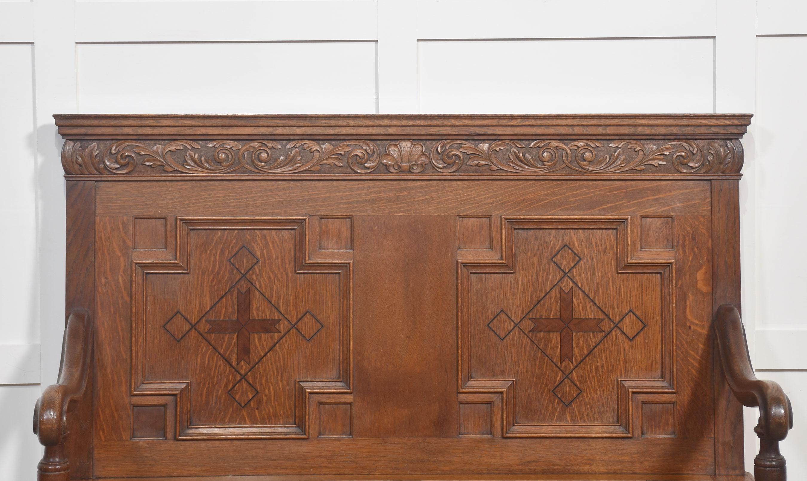 A fine quality antique oak settle, crafted with traditional detail and solid construction. The high backrest is decorated with deep panel mouldings and striking inlaid geometric motifs, framed by a beautifully carved top rail with scrolling foliage