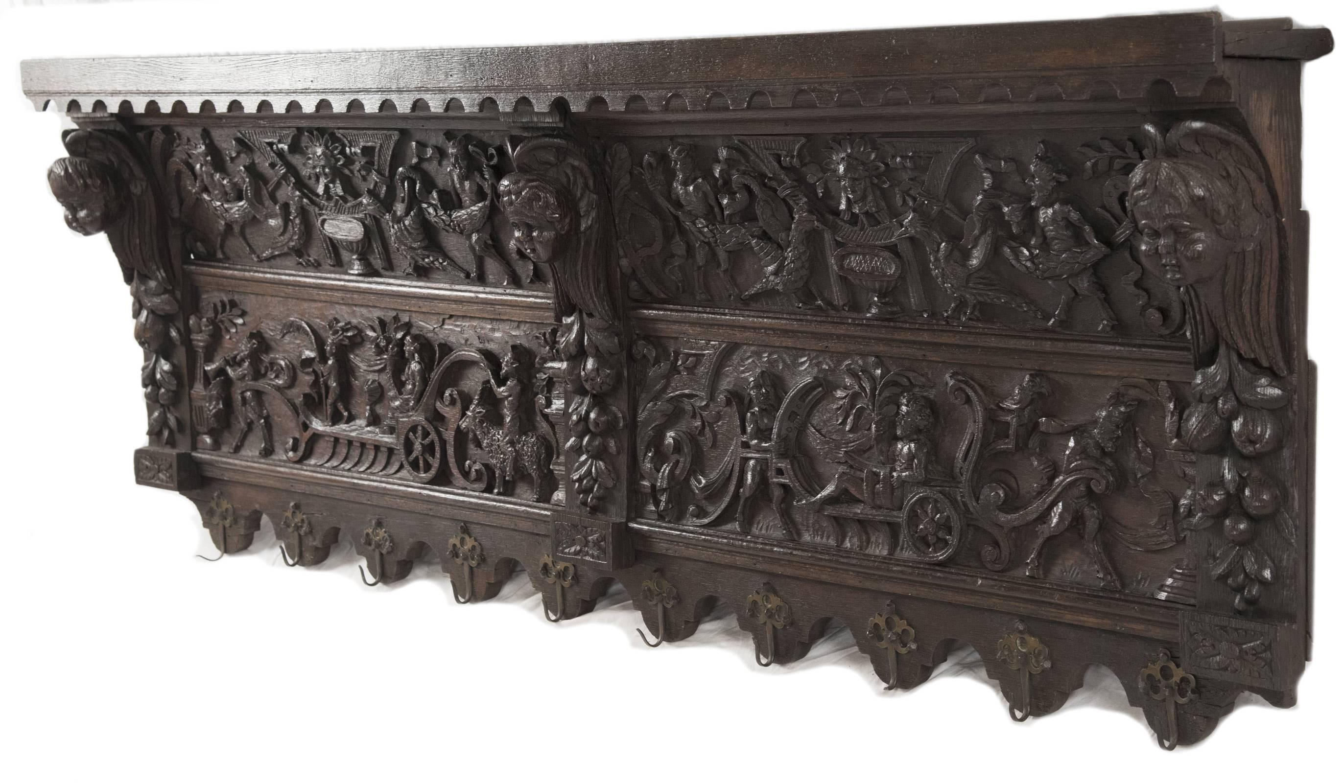 A 19th century French oak shelf with brass hooks, carved in high relief with images of centaurs, men and beasts in a procession celebrating the harvest, the decorative panels flanked by winged putti and garlands of fruit. Measures: 23 x 61 x 6 ½