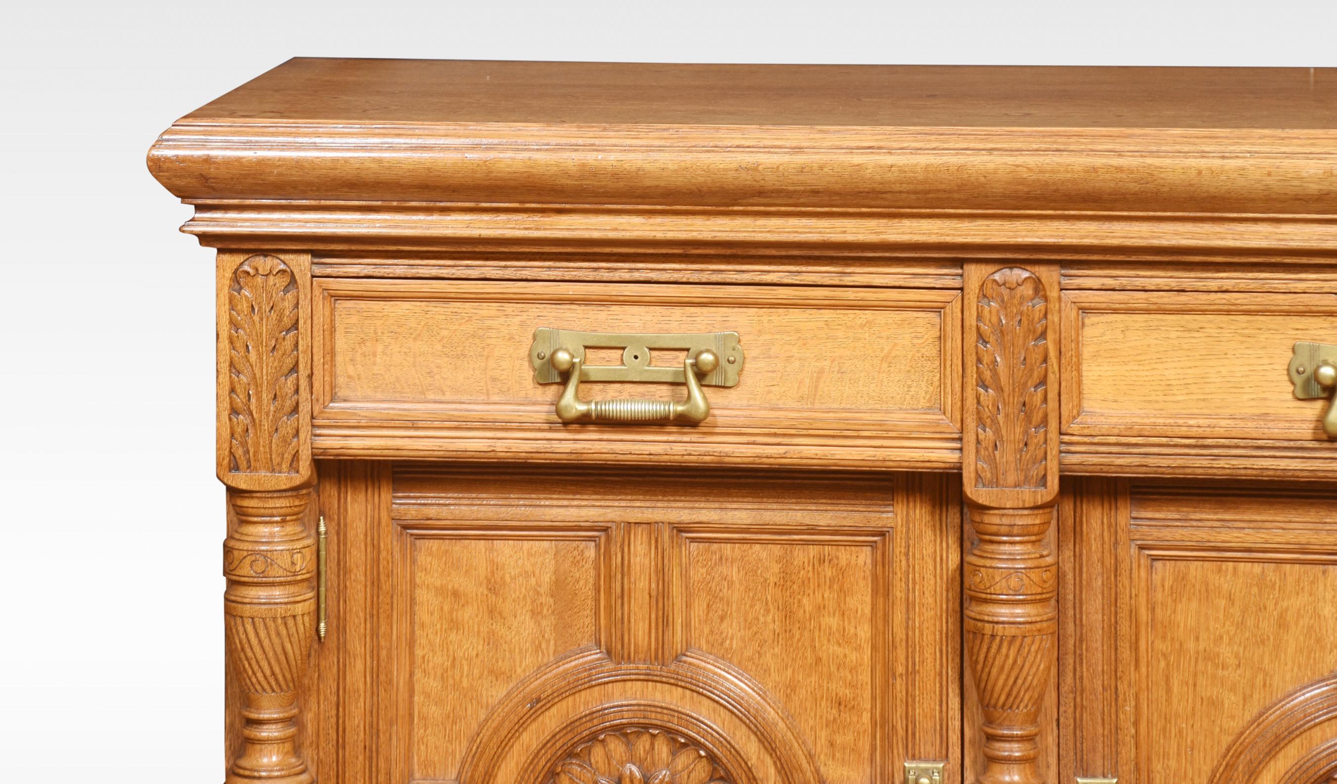 19th-century oak sideboard, the large rectangular top with moulded edge above two freeze drawers fitted with bold brass handles. The base section is fitted with a pair of panelled doors with circular moulded centres with floral carved decoration.