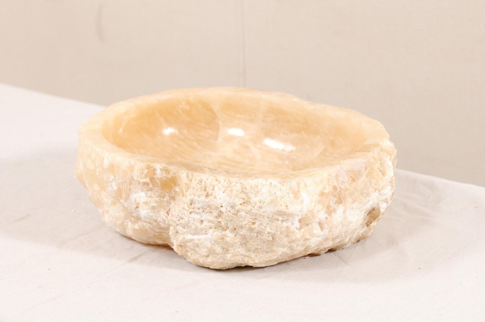 A single natural onyx sink basin with original live edge. This carved vessel sink, created from a rough onyx rock, has a carved and then polished interior basin, making for easy clean-up. The natural textured stone remains about the exterior of the