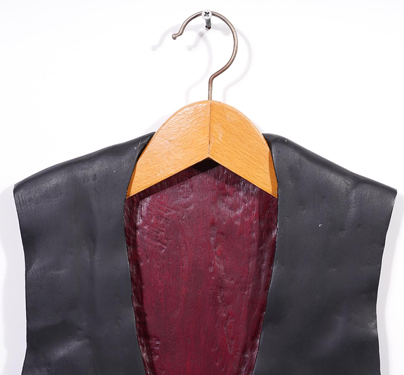 This carved and painted wood sculpture representing an old fashioned mans vest mounted on a regular looking hanger is painted in black and burgundy red and is signed illegibly and dated 1986. I am a great addition to an artsy home or a collection of