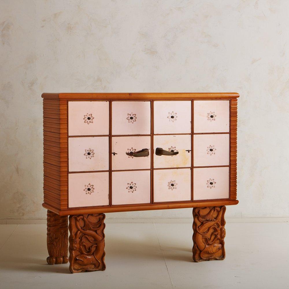 A stunning 1930s Italian bar cabinet designed by Osvaldo Borsani. This piece was constructed from bleached pear wood and stands on four rectangular legs with intricate hand carved fish and marine motifs. Two bi-fold doors feature rose hued mirrored