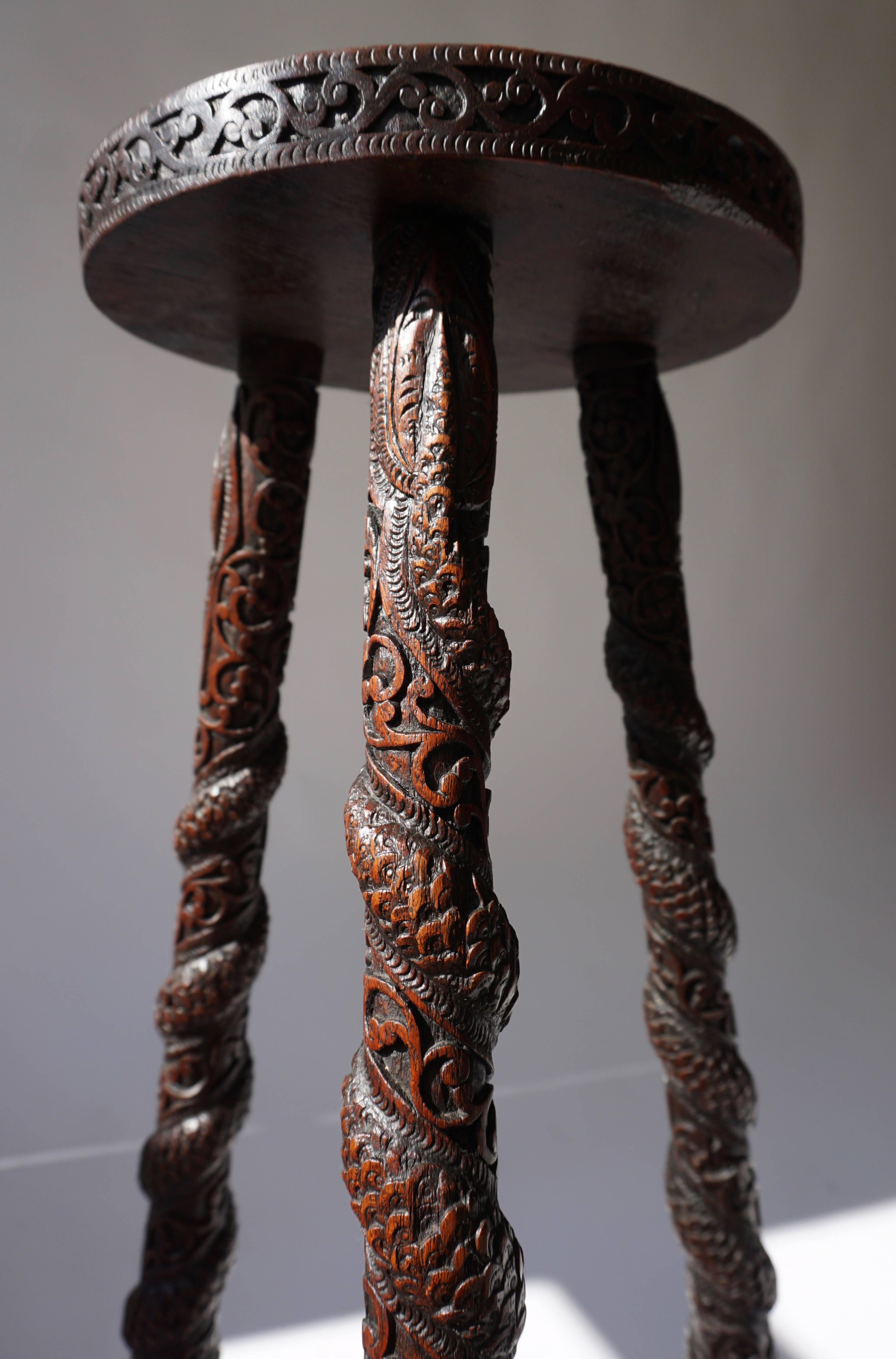 A Burmese hardwood tripod stand, carved all over with scrollwork and flowers, the legs with dragons spiralling down amidst curly branches. The central medallion represents Burmese dancers. 20th century.