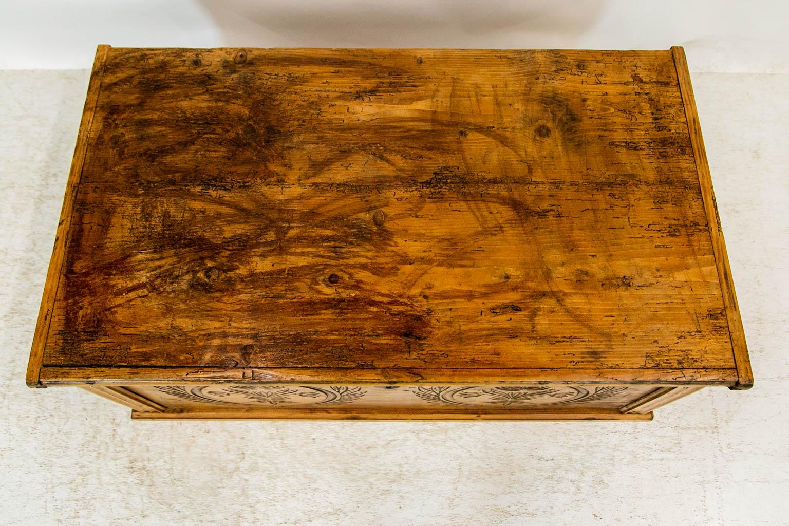 This blanket chest has the original rattail hinges, steel lock, keyhole escutcheon, and lifting handles. The inside has a candle box with a lift top lid. The front has incised carvings with a floral wreath motif. The top has old exposed past insect