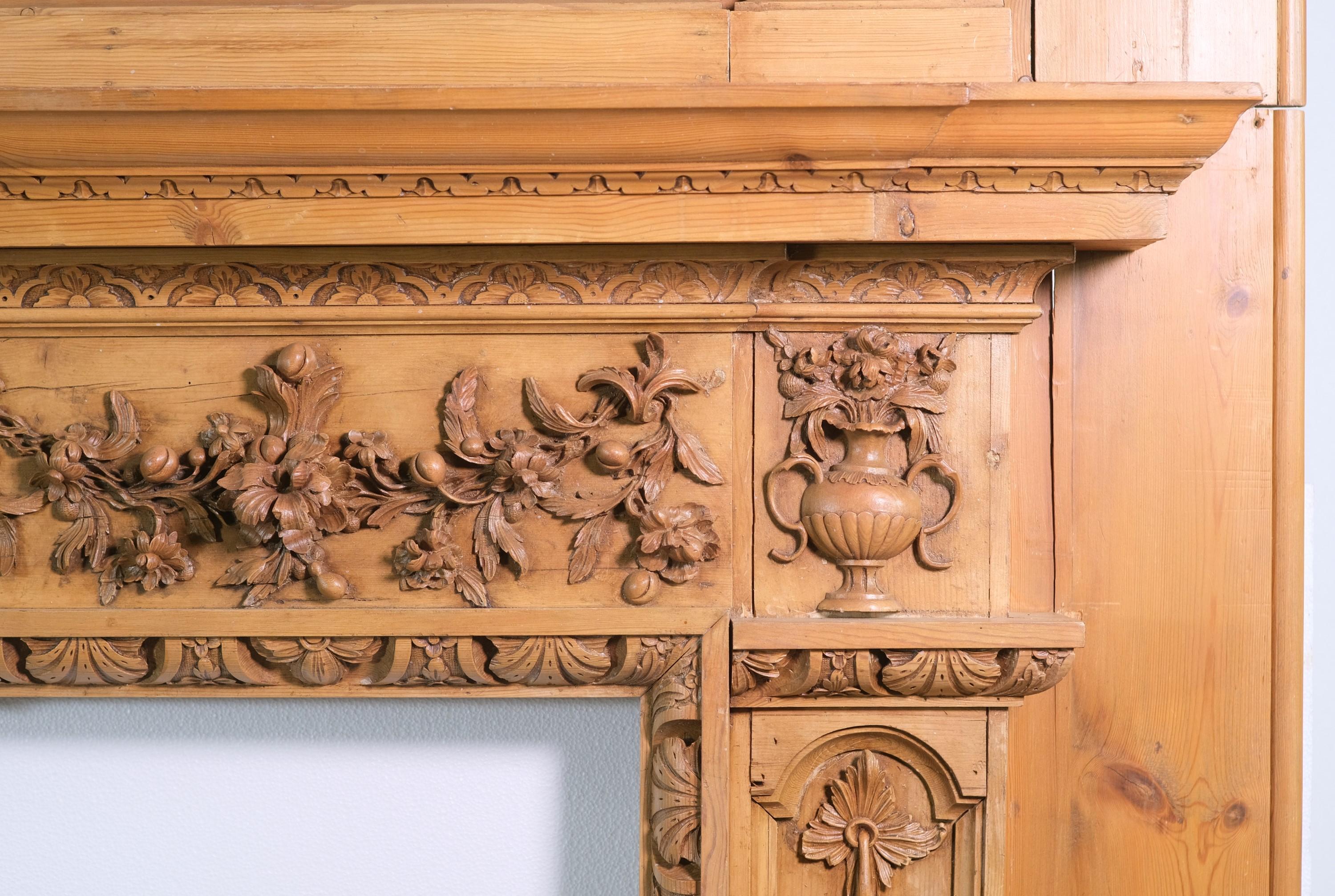 Rare vintage Rococo pine mantel with a natural finish and highly carved molding, and applied floral with urns throughout. There is some minor chipping and missing design elements. There is a carved out hole in the center panel. Please see the