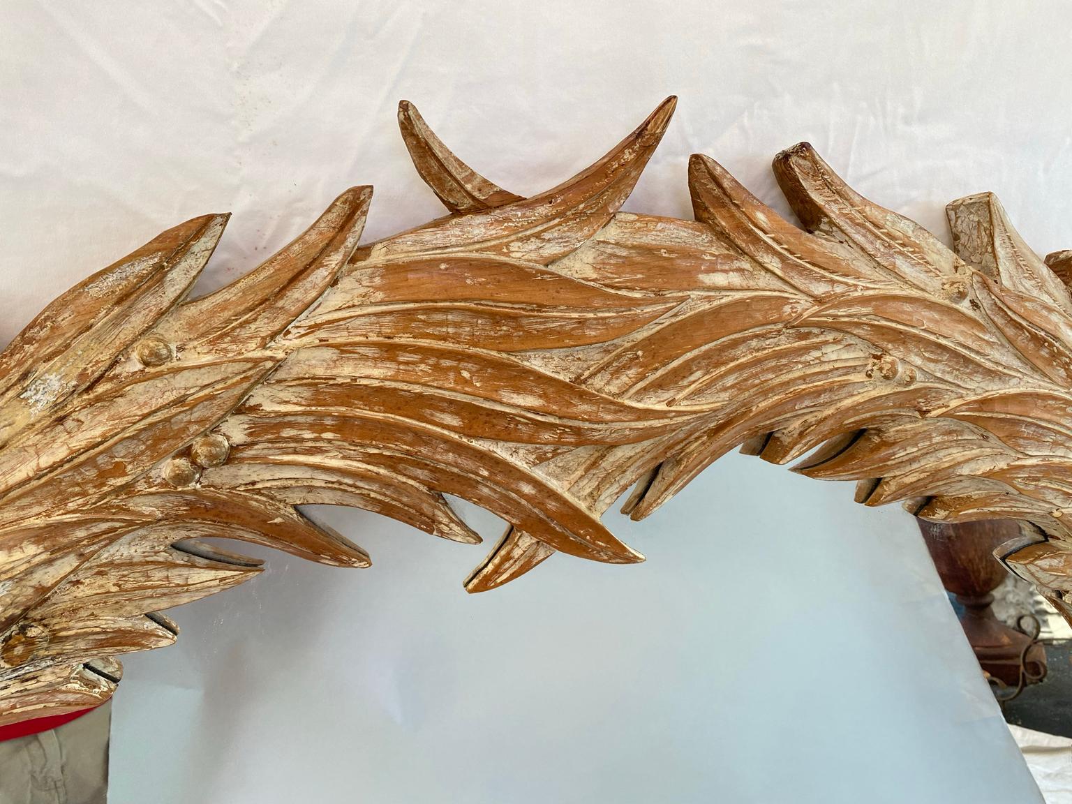Wall mirror, of pine, having a pickled finish, its arched frame carved with elaborate palm leaves, a crossed ribbon adorns the center of the mirror's bottom. 

Stock ID: D9296.