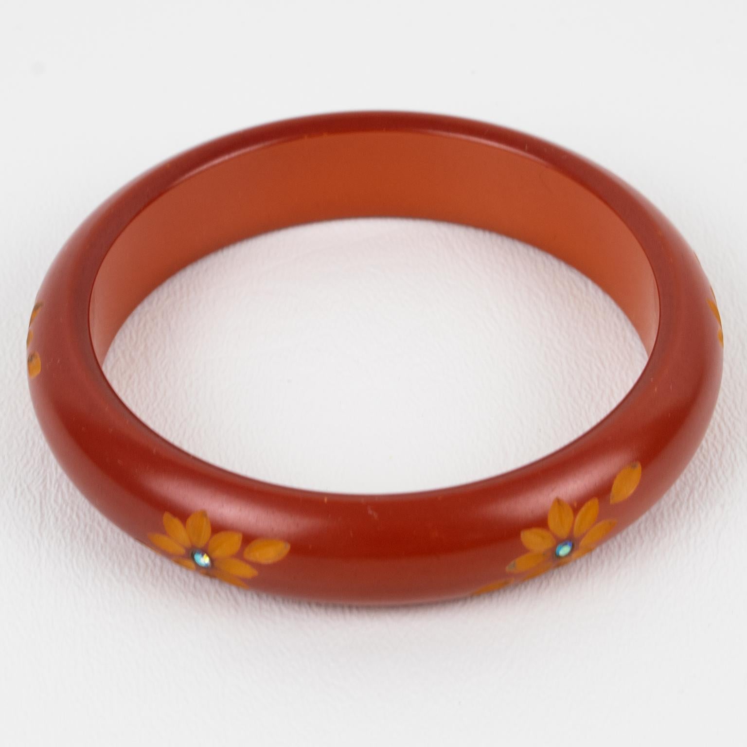 Voici un superbe bracelet en bakélite sculpté de style Art Déco. La forme bombée massive est entourée de profondes sculptures florales et est ornée de minuscules strass AB en cristal. La pièce présente une couleur rouge-rouille intense avec un