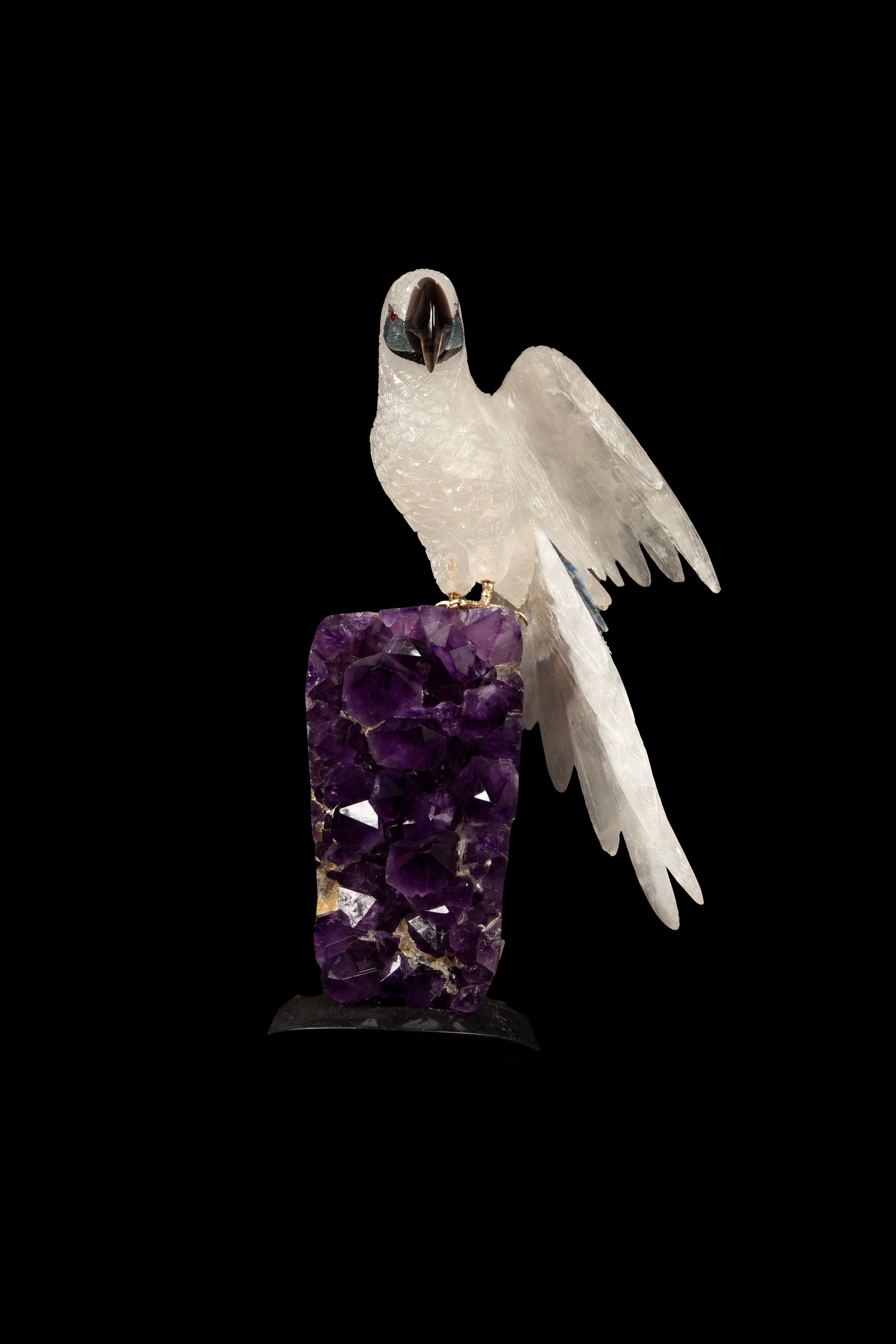 This exquisite 13-inch high carved rock crystal parrot, meticulously handcrafted in Argentina, presents a stunning depiction of artisanal craftsmanship. Perched atop a vibrant amethyst cluster, the sculpture captures the essence of natural beauty