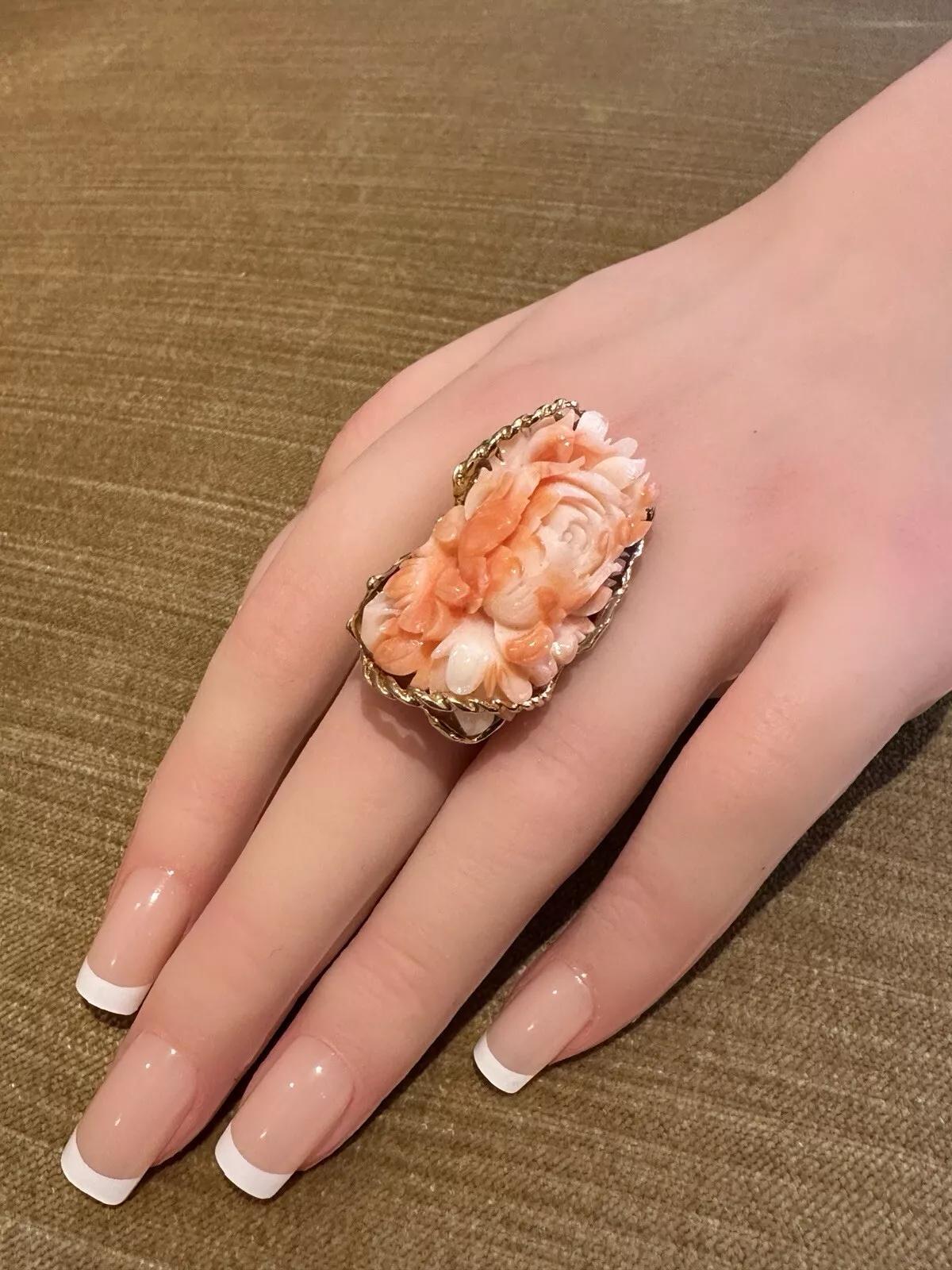 Carved Rose Angel Skin Coral Ring in 18k Yellow Gold 

Carved Coral Ring featuring Elongated piece of Angel Skin Coral carved in a Rose motif set in 18k Yellow Gold.

The angel skin coral measures 1.50 inch by .75 inch.

Ring is size 7.5
Ring top