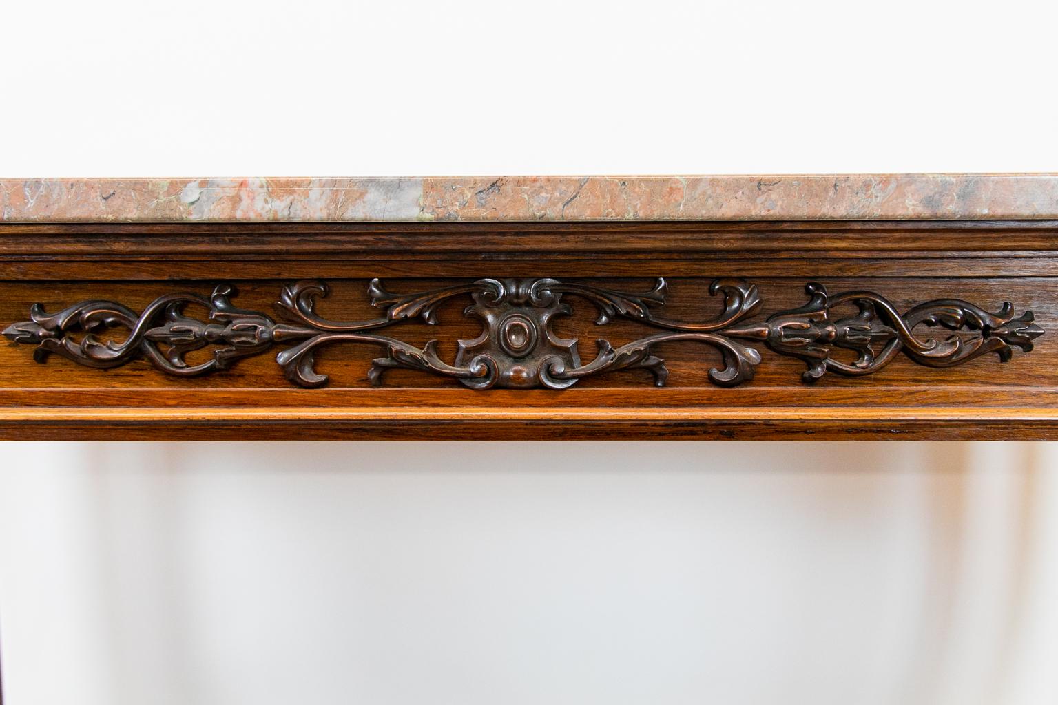 Carved rosewood English marble-top console table, with the marble having soft earth tones. The apron with central bellflower and floral appliqué in high relief, oval rosettes at each end. The front legs are fluted and reeded and terminate in