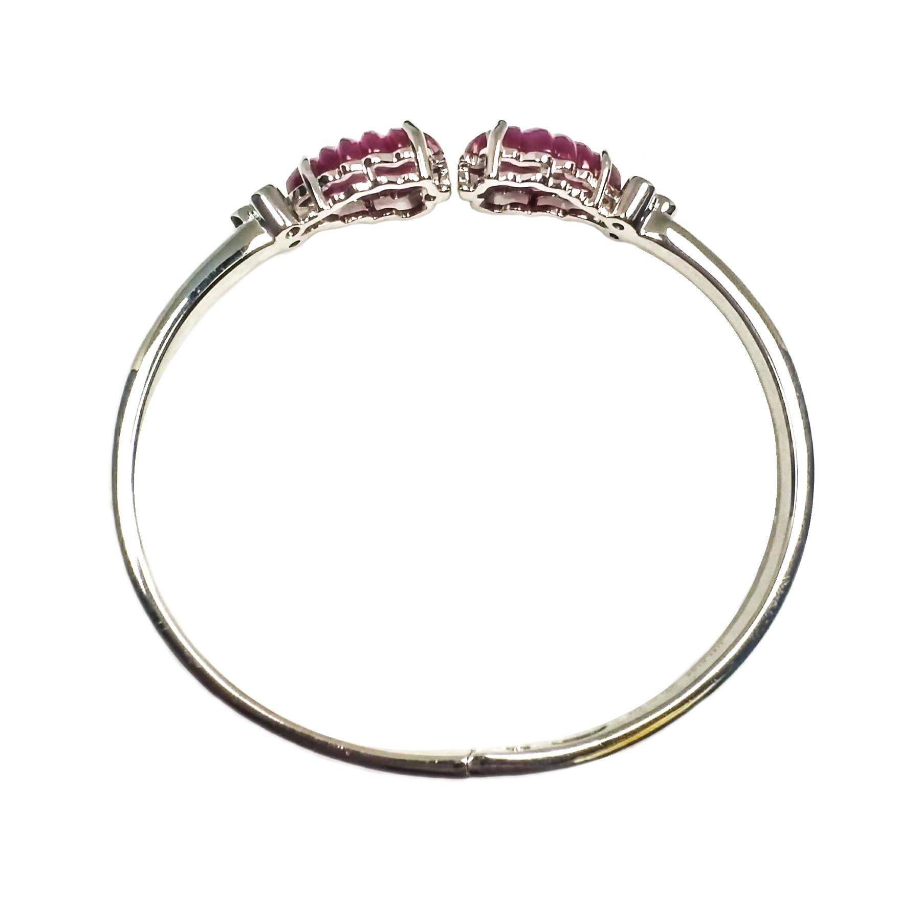 Carved ruby and diamond bangle. Lively red, two matching leaf carved rubies, set in open basket profile with four prongs, accented with round brilliant cut diamonds. Beautiful high polished bangle set in 14 karat white gold, with hinged clasp.