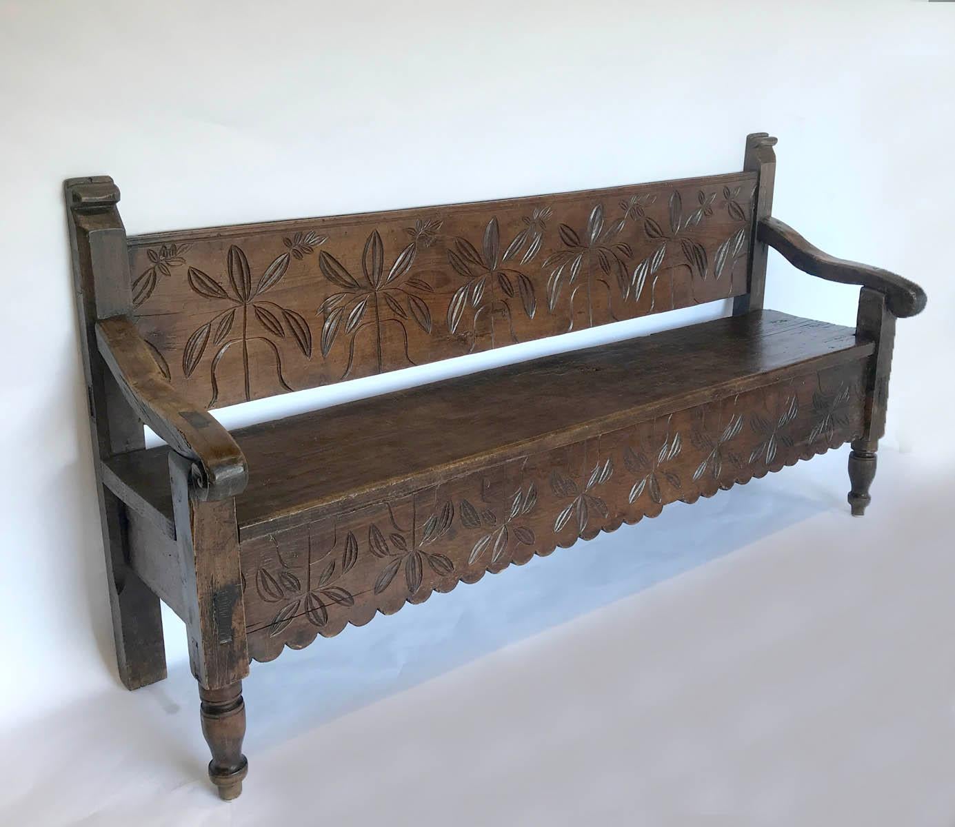 Rustic bench with carved back and apron. Scalloped apron and turned from legs. Hand hewn back and seat. Spanish Colonial style. Very sturdy. Can go outside if it is under cover. Cipres (Cypress) wood.