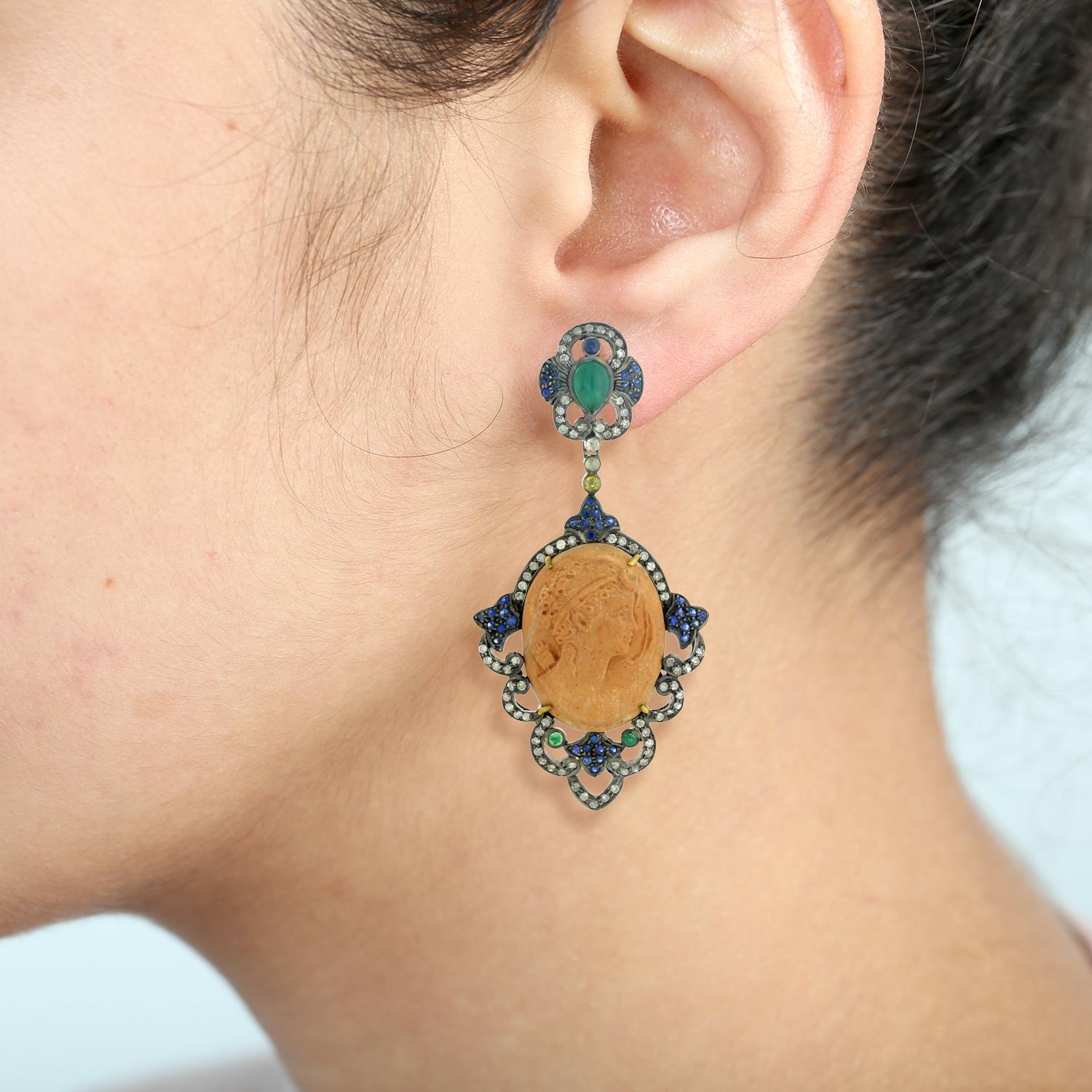 Adorn yourself with the timeless beauty of these Carved Shell Cameo Earrings with Emeralds, surrounded by Pave Sapphire & Diamonds. Featuring intricate shell carving, these earrings showcase a stunning oval cameo design, surrounded by a halo of
