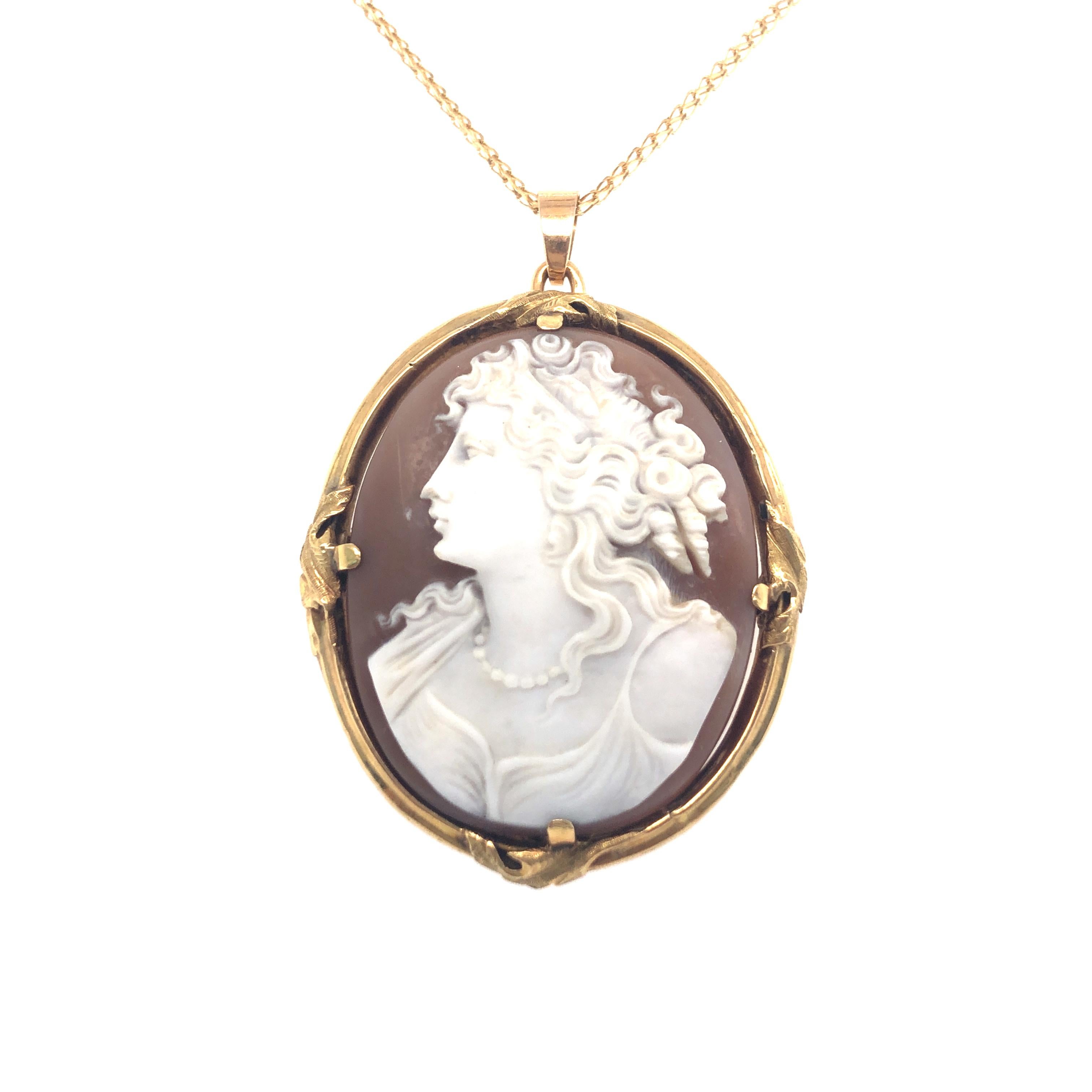 This hand-engraved shell cameo depicts a figure with a classic profile, upswept curly hairdo and flowing robe. The neck is adorned with a classic pearl necklace.
The two-coloured cameo is held by four prongs in a delicate setting decorated with