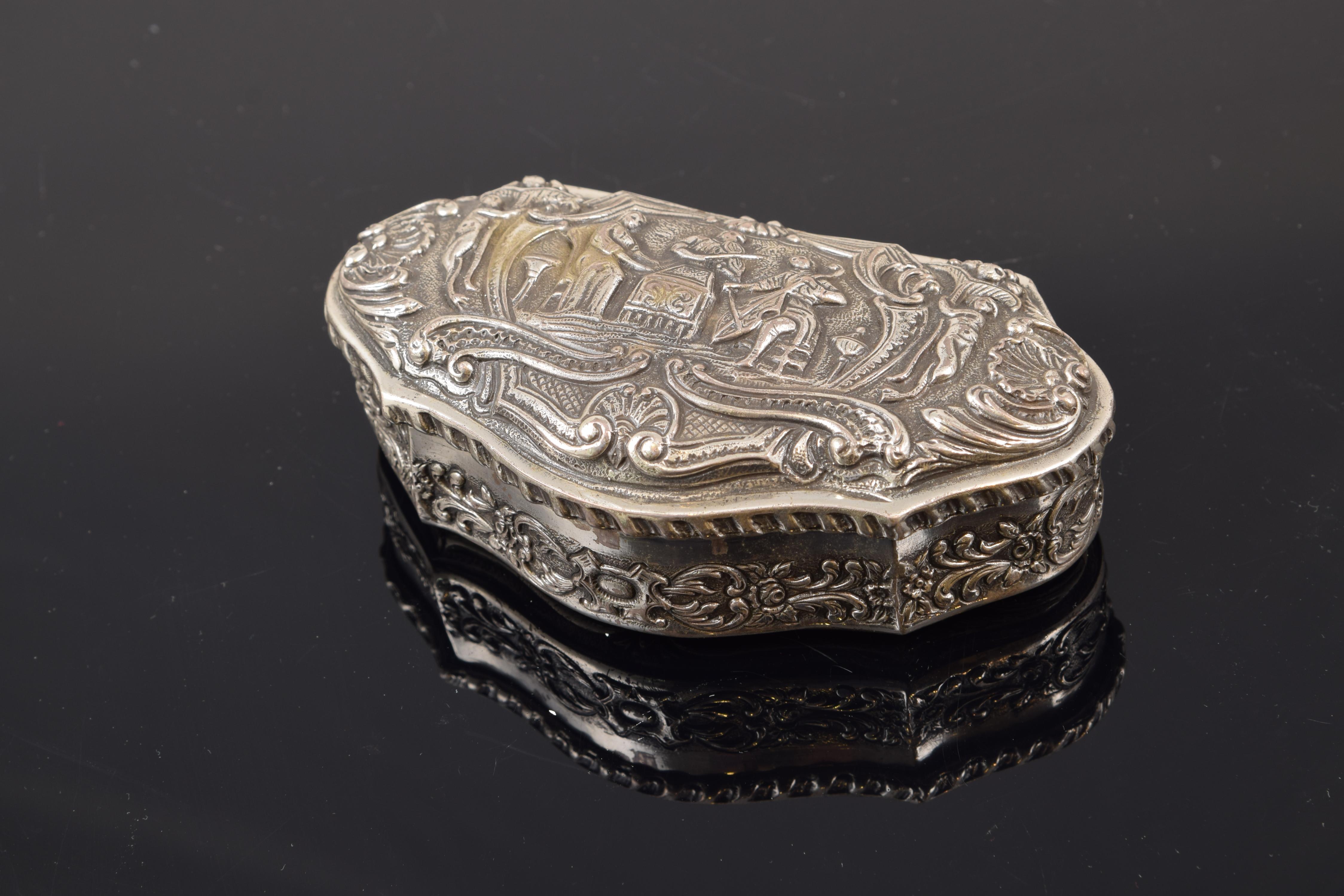 Carved silver box, 20th century. 
 Small silver box carved with a great variety of motifs, all belonging to different artistic traditions based on Roman classicism. On the cover, there are two musicians framed in a decoration formed by figures and