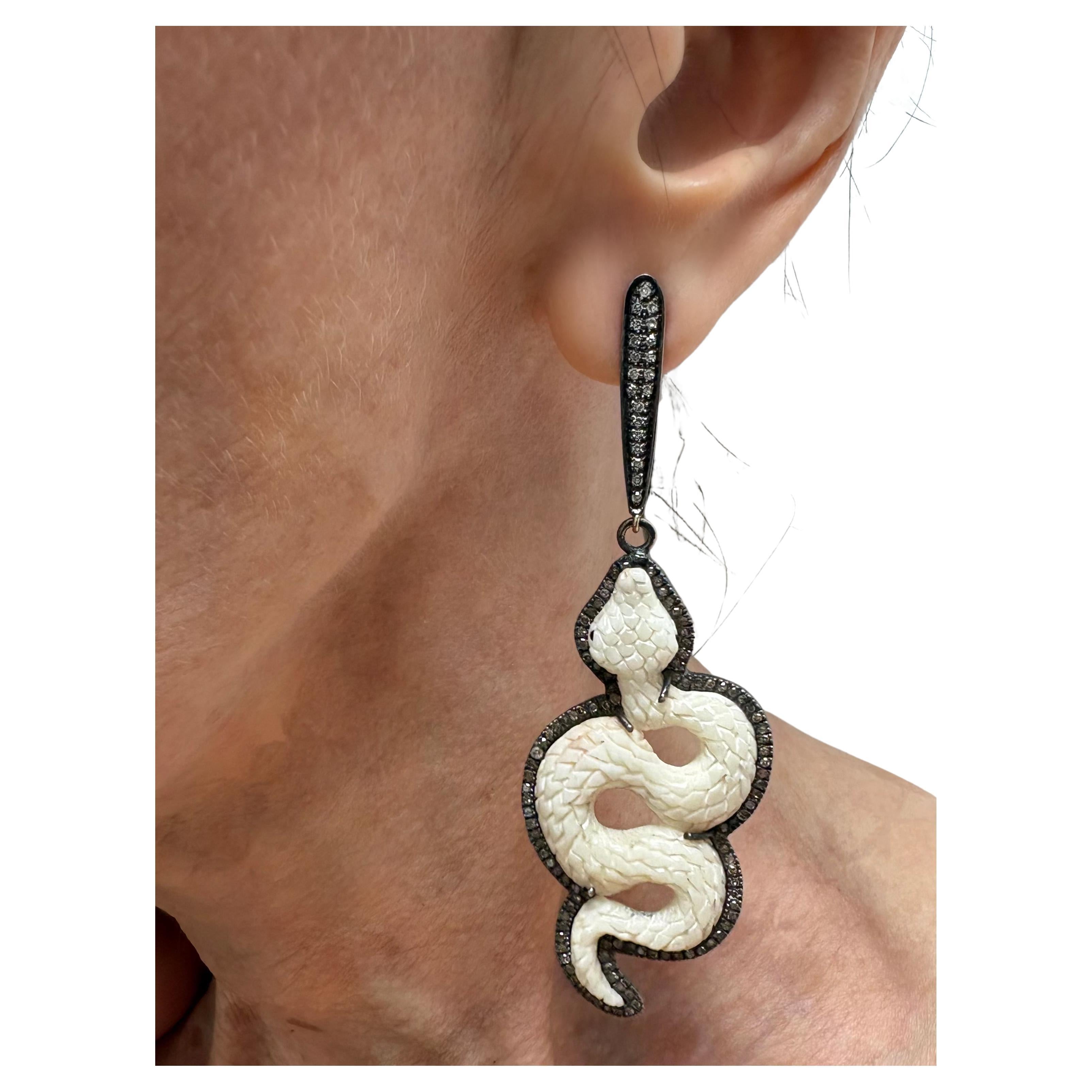 Description
These captivating snake earrings entwine primal beauty with daring edgy style. Sculpted from polished bone, their sinuous forms reflect grace and power. The interplay of shimmering diamonds encircling the organic carved snakes exudes an