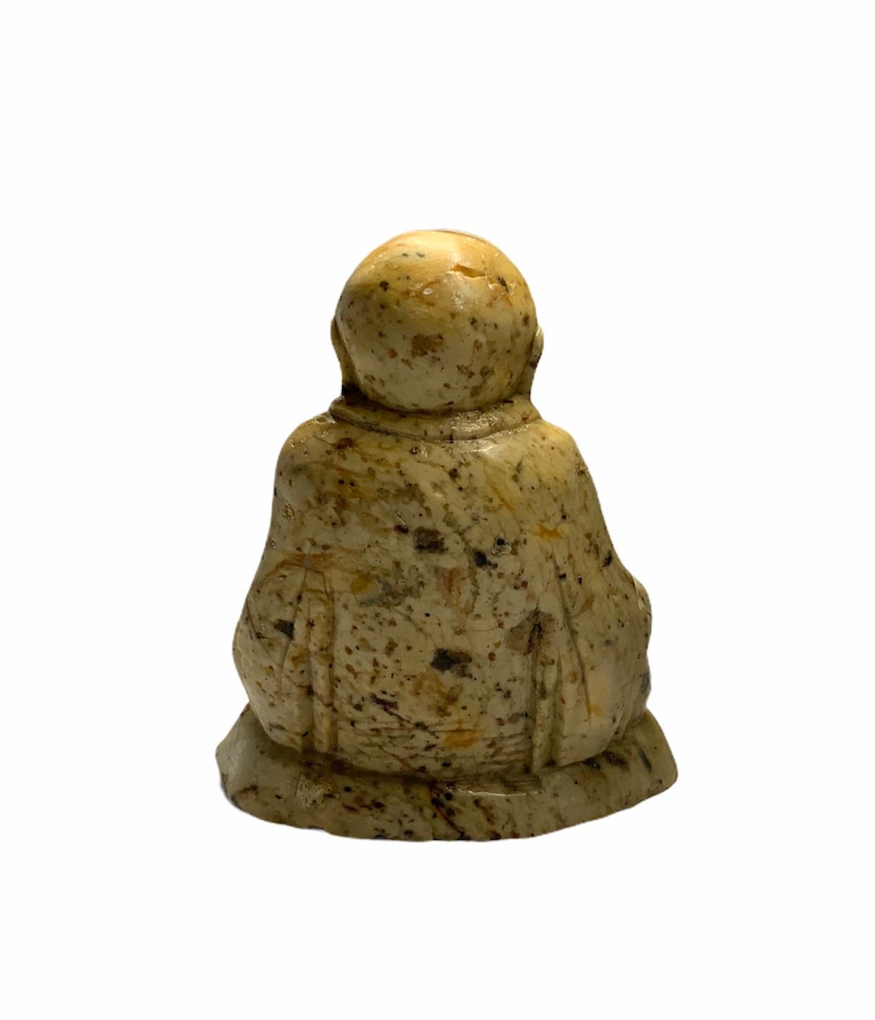 Dieser schwere geschnitzte Buddha aus hellgelb-grünem Speckstein sitzt auf einem ovalen Steinsockel mit Klammerfüßen.