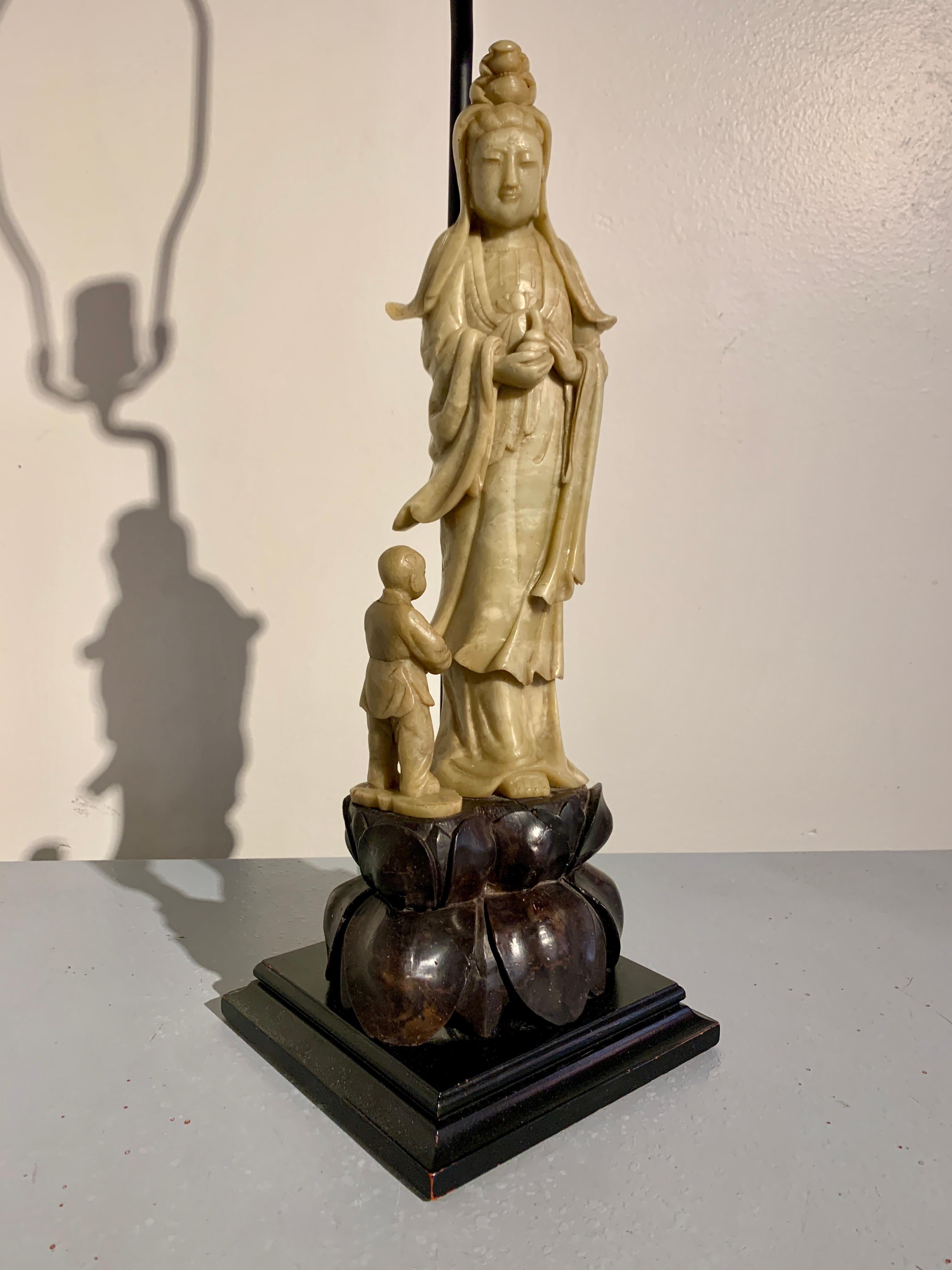 A beautiful and elegant carved soapstone figure of Guanyin and attendant, now mounted as a table lamp. The soapstone carving circa 1940's or earlier, China, mounted as a lamp in the 1960's, USA. 

Carved of a waxy soapstone, Guanyin, the bodhisattva