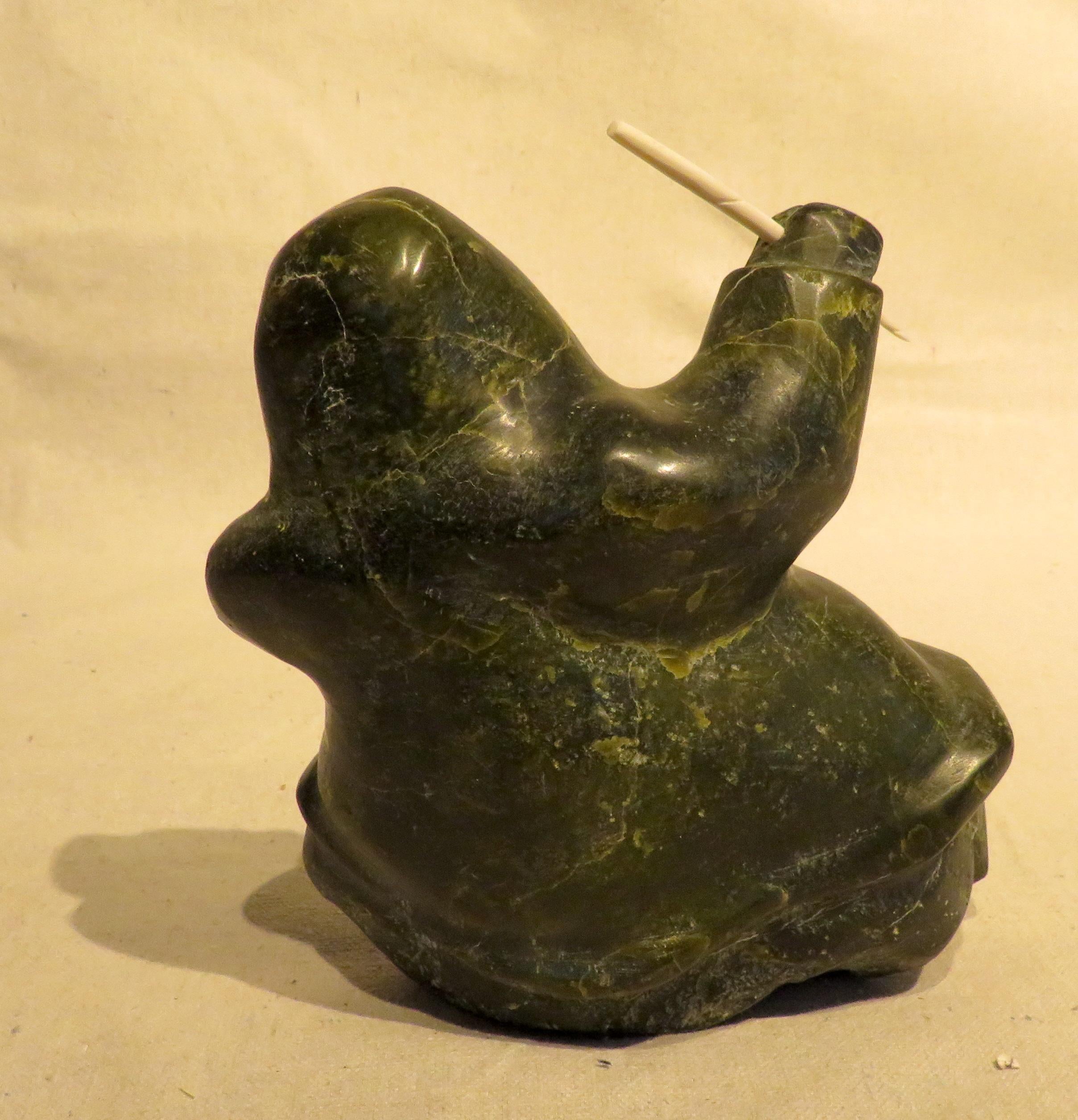 Carved Black Soapstone of Seated Inuit figure, holding a carved bone Narwhal tusk in one hand and a carved bone fish in the other.