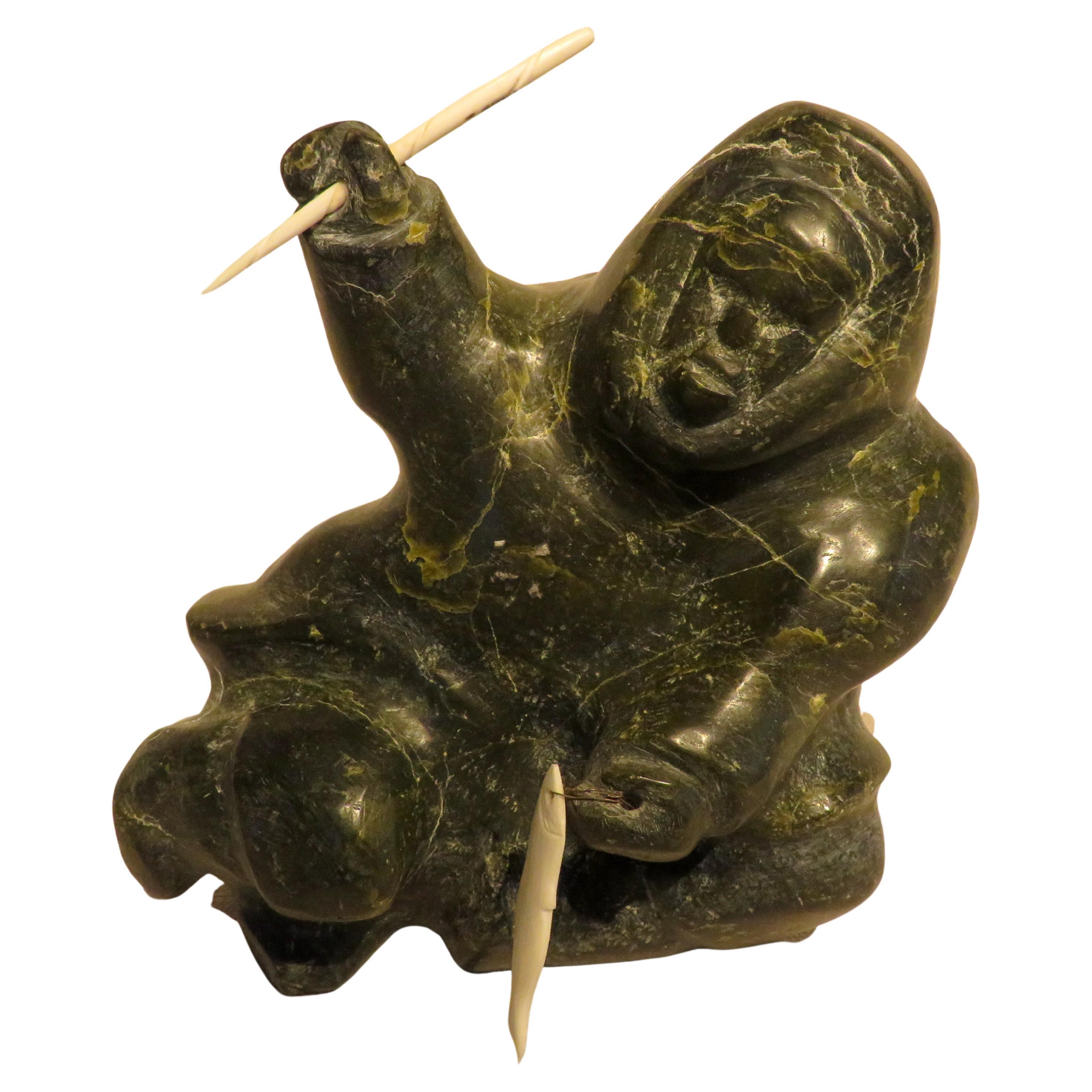 Geschnitzte Seifenskulptur eines sitzenden Inuits aus Knochen, der einen Narwhal-Schreibtisch und einen Fisch hlt