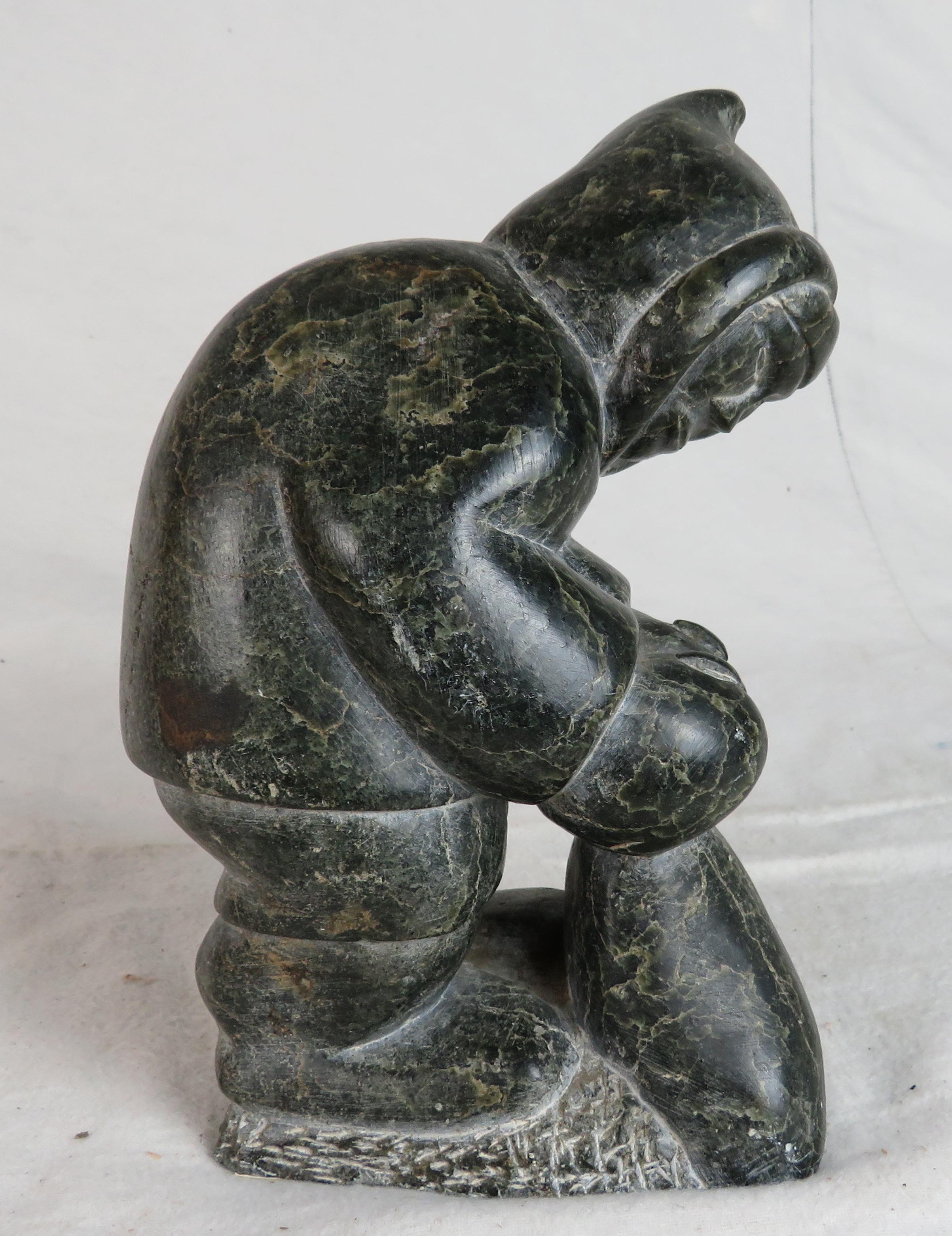 Carved Black Soapstone Inuit figure stooped over, grasping a bag at his feet.