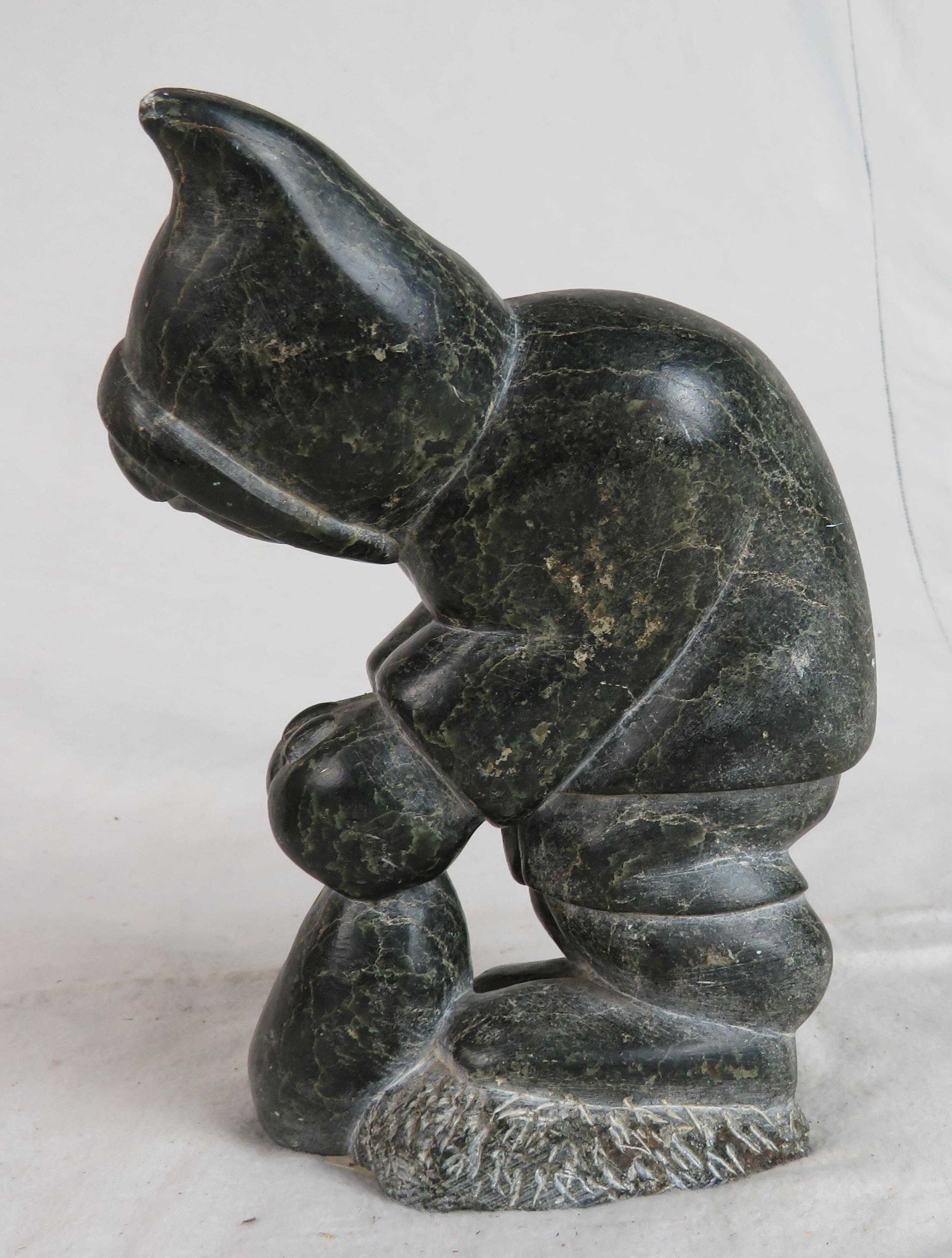 Canadien Sculpture en grs sculpt d'un Inuit se penchant vers l'avant, tenant un sac  pieds en vente