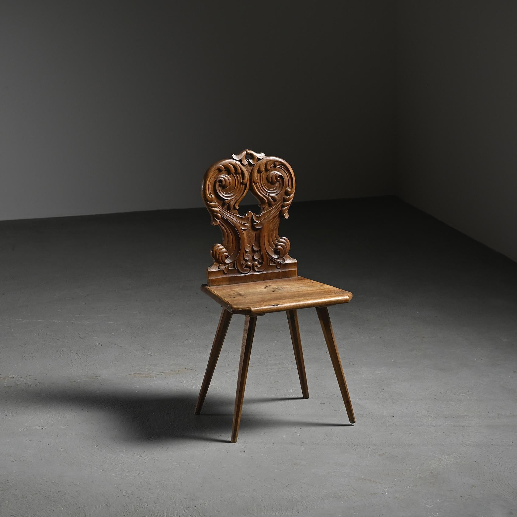
Solid wood escabelle with an openwork backrest featuring symmetrical scrolls and a central spade-shaped cutout. The ornamentation, rooted in Alpine folk art, combines traditional symbolism with rustic elegance.

The faceted seat stands on four