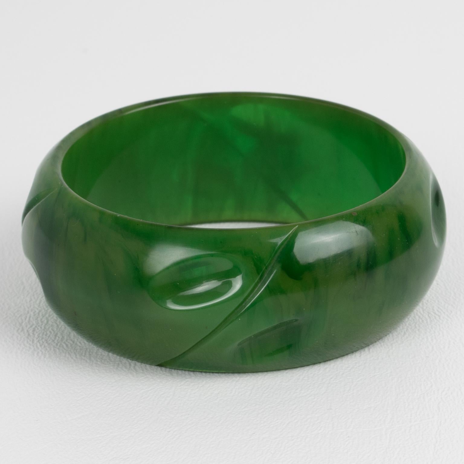 This is a stunning, green marble Bakelite carved bracelet bangle. It features a chunky, domed shape with a geometric carving design. The color is an intense green marble tone with cloudy swirling. 
Measurements: Inside across 2.63 in diameter (6.6