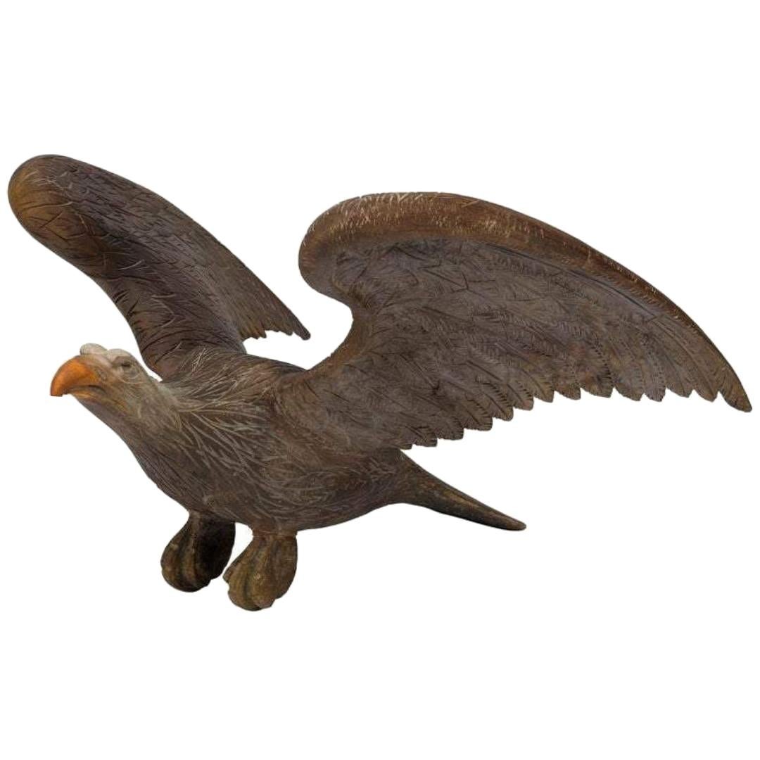 L'aigle présenté est un aigle à ailes déployées, datant très probablement de la fin du XIXe ou du début du XXe siècle. Cet aigle en pin sculpté est prêt à décoller et présente des détails faciaux féroces et un plumage bien sculpté. L'aigle sculpté