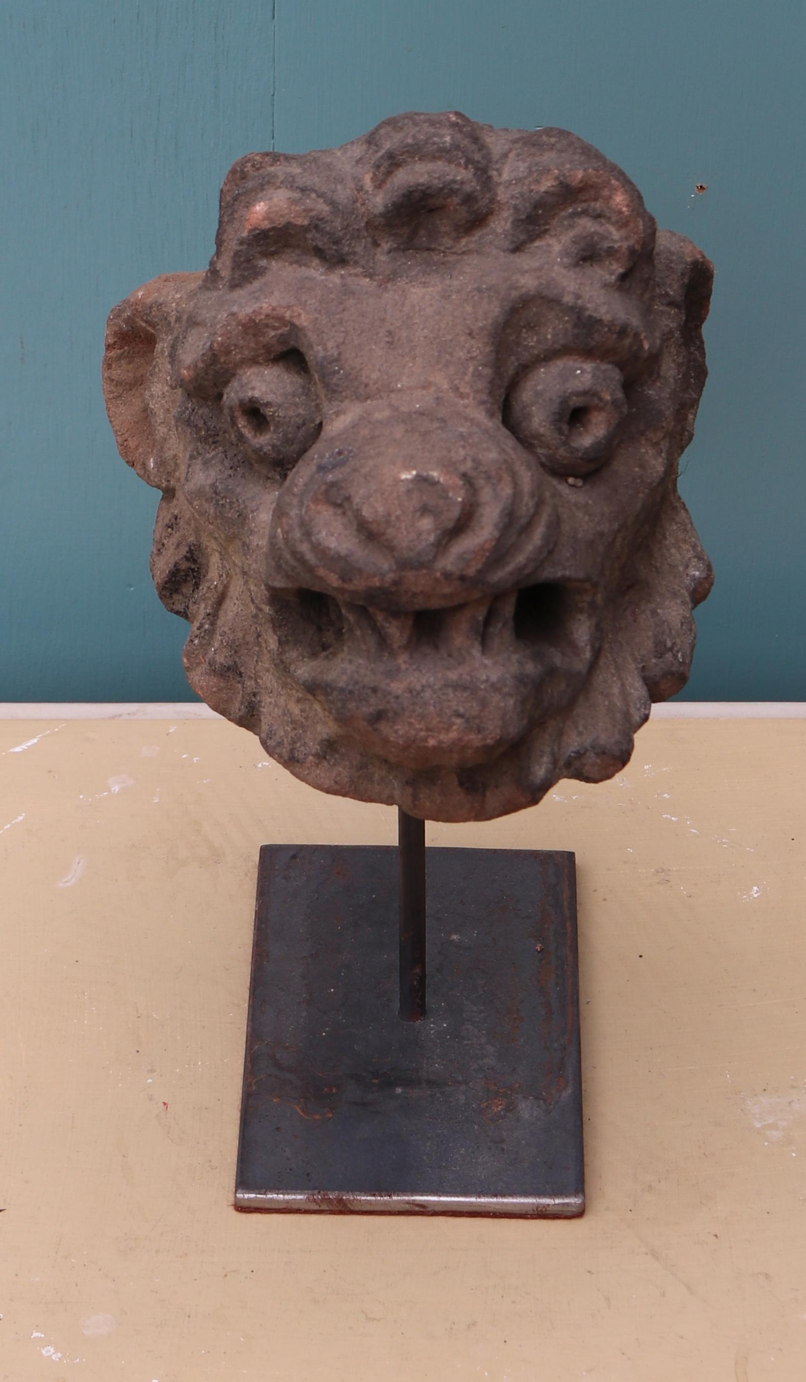 A reclaimed carved sandstone head of a lion, mounted to a steel display stand.