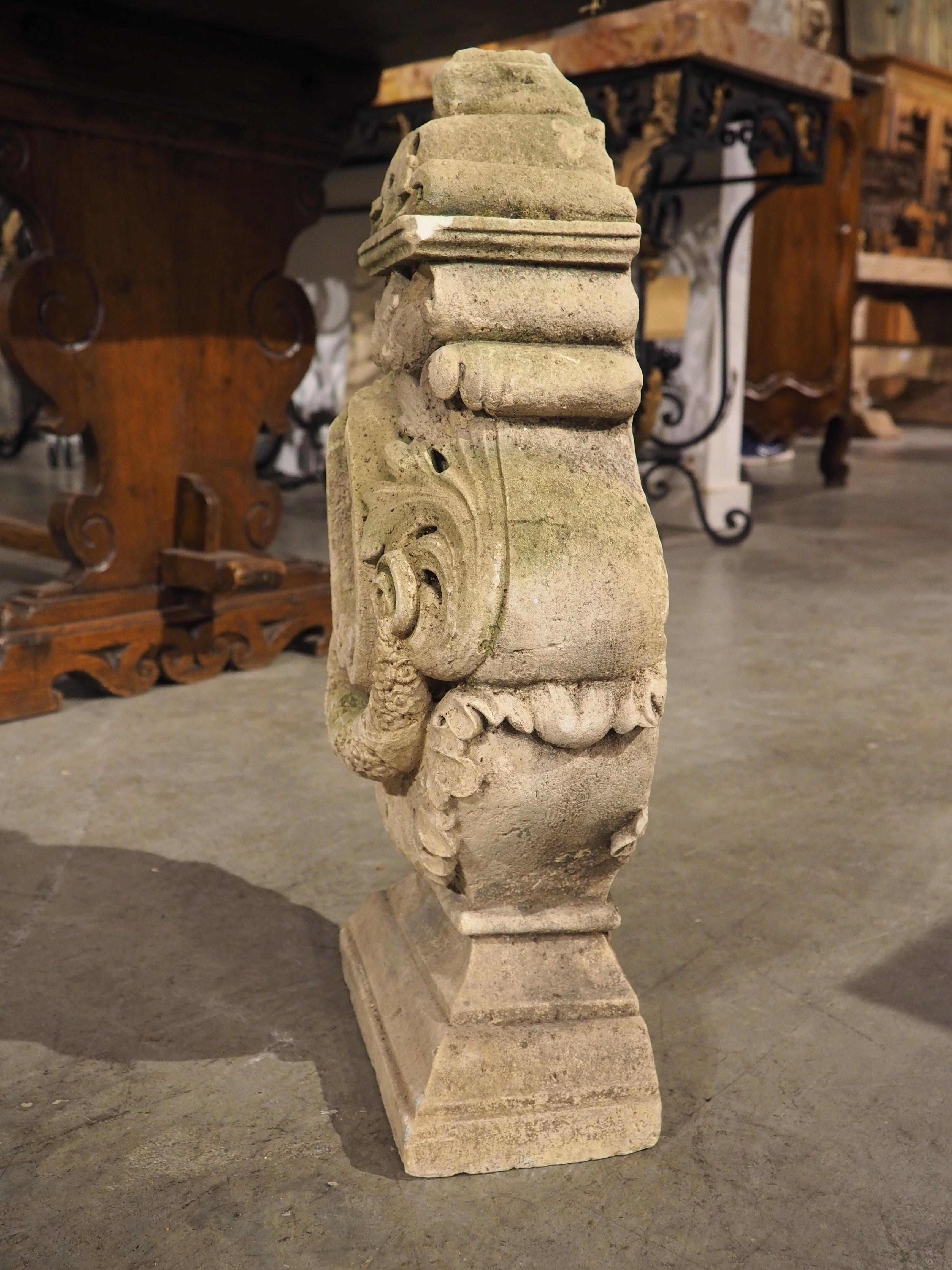 Sculptée à la main en France, vers 1850, cette architecture unique en pierre calcaire rappelle un reliquaire antique. Son design complexe présente une niche centrale flanquée de volutes, au-dessus d'une guirlande florale qui tombe en cascade sur une