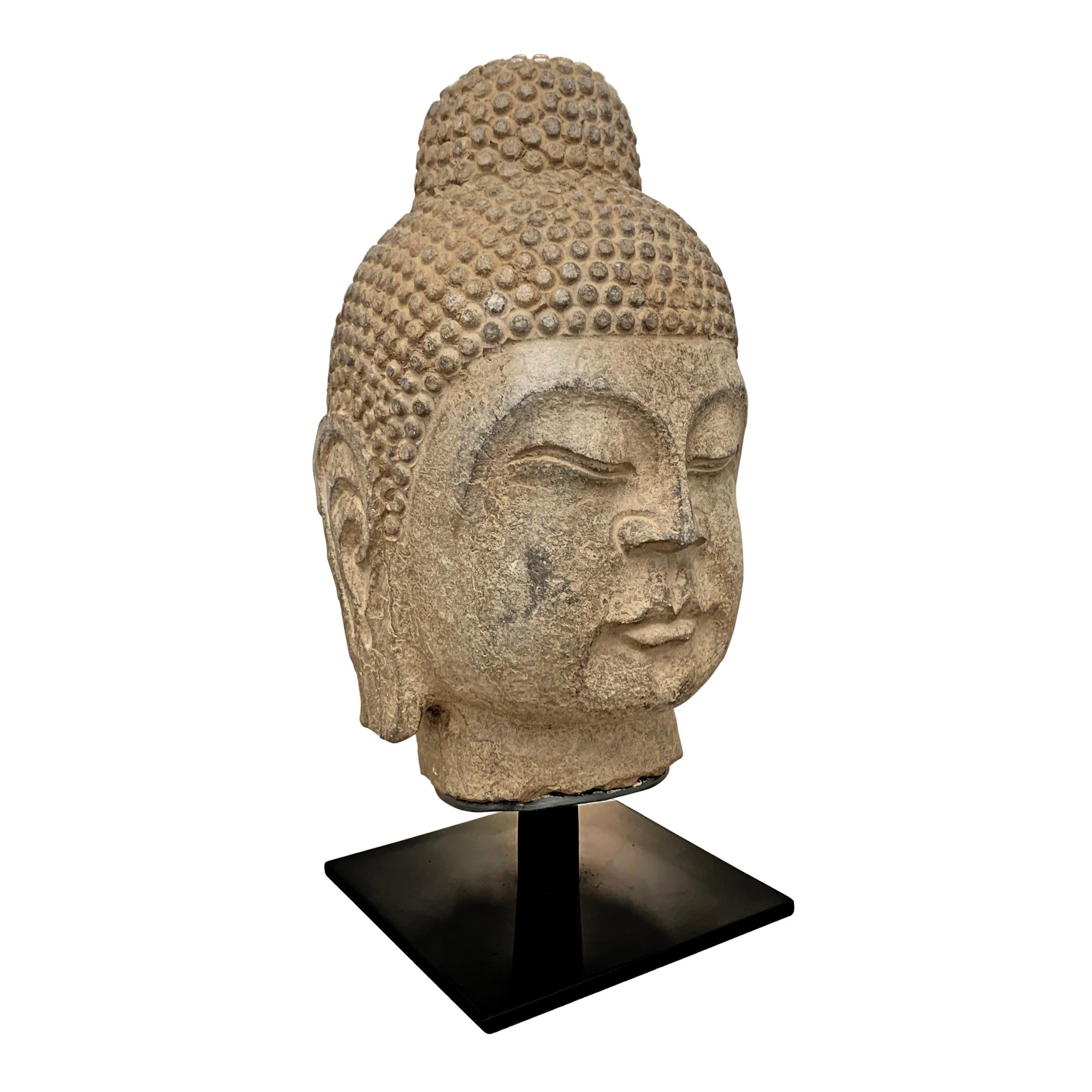 A beautiful carved limestone Buddha head with a serene contemplative expression, on a custom steel mount.