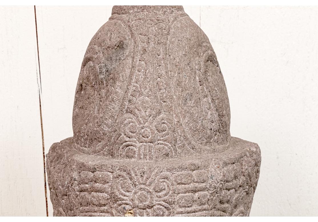 Grand buste bien sculpté en pierre dure rougeâtre représentant le Bouddha aux yeux fermés et à l'expression sereine. Le Bouddha porte une grande et complexe coiffe de forme traditionnelle et une queue de cheval bouclée en spirale dans le dos.