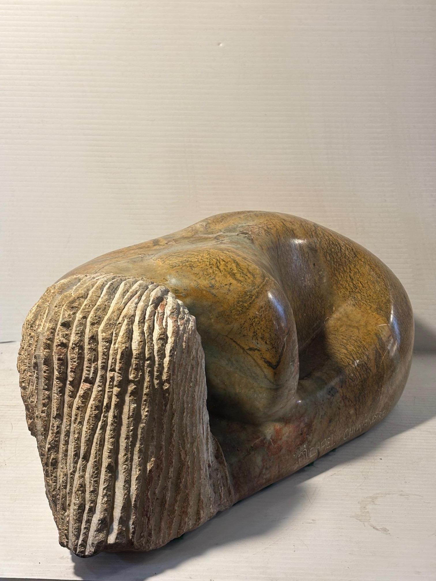 Diese schwere polierte Steinskulptur des bekannten Bildhauers Michael Chiwandire zeigt eine zusammengerollte Frauenfigur. Ihr Haar hat ein auffälliges und raues Aussehen. Die Signatur des Künstlers ist auf der Seite eingeritzt.
Bitte bestätigen Sie