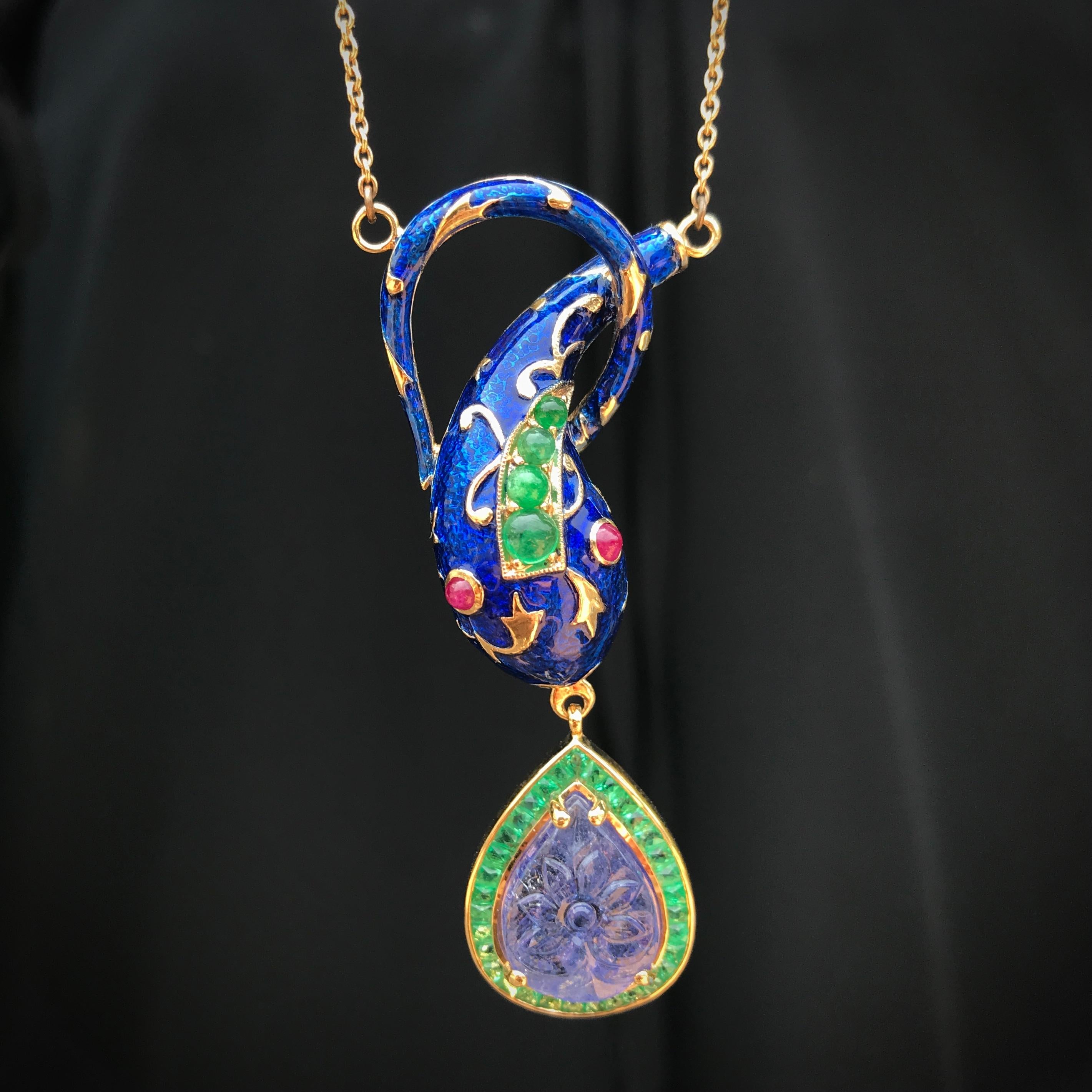 A beautiful and very wearable snake necklace has a friendly face with ornate blue enamel, engraving on the gold, cabochon ruby eyes and cabochon emerald on its her head. Hanging from her mouth is a beautifully carved pear shaped tanzanite surrounded