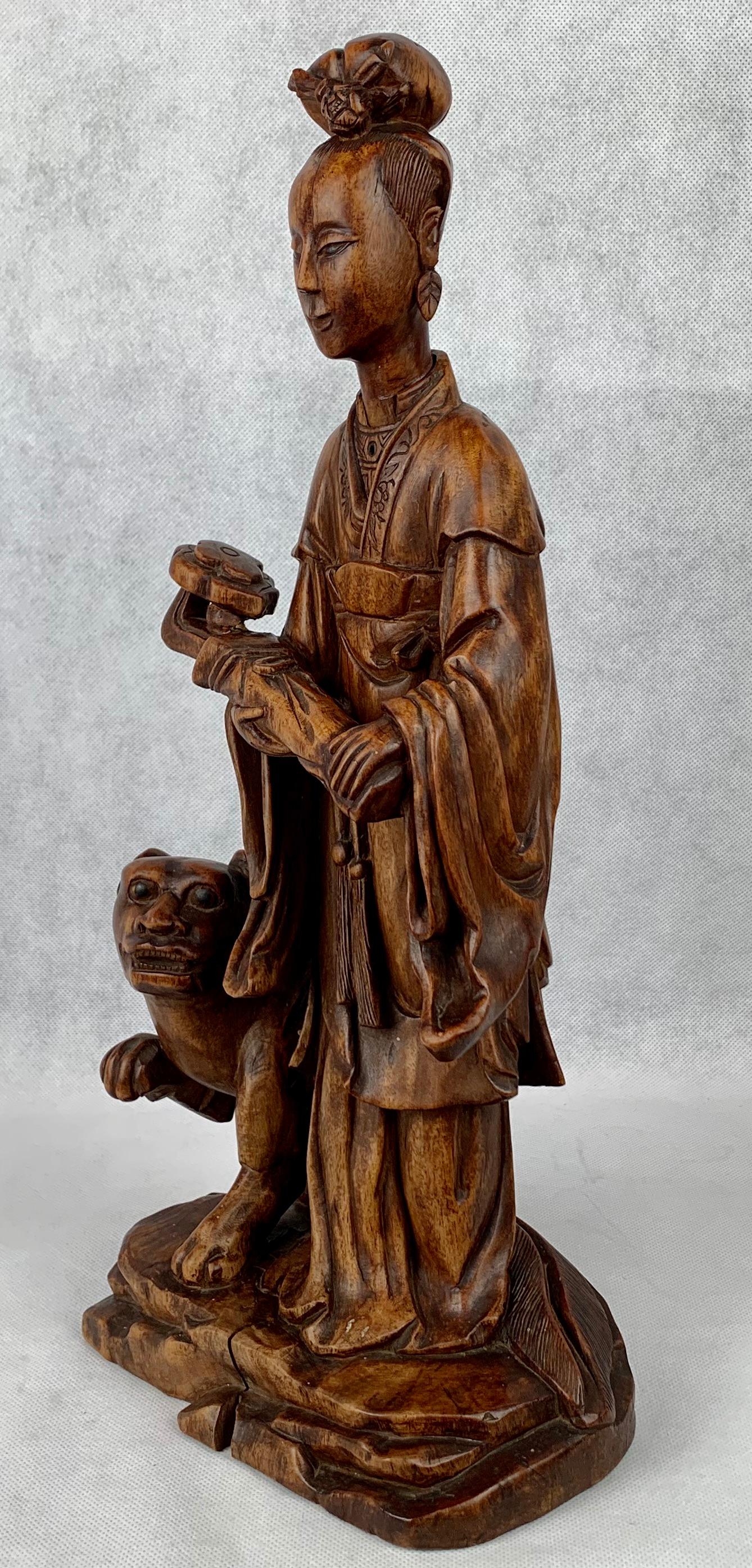 Figure féminine chinoise en teck sculpté tenant un Ruyi (sceptre) dans ses mains avec un chien à ses pieds. La figurine est dans un état solide et très robuste.  La tête est amovible.  Il y a quelques stries d'âge et une fente dans la base