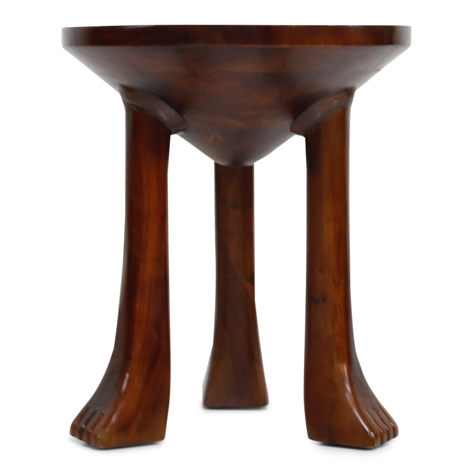 These attractive three-legged carved teak side tables are in the style of John Dickinson's 