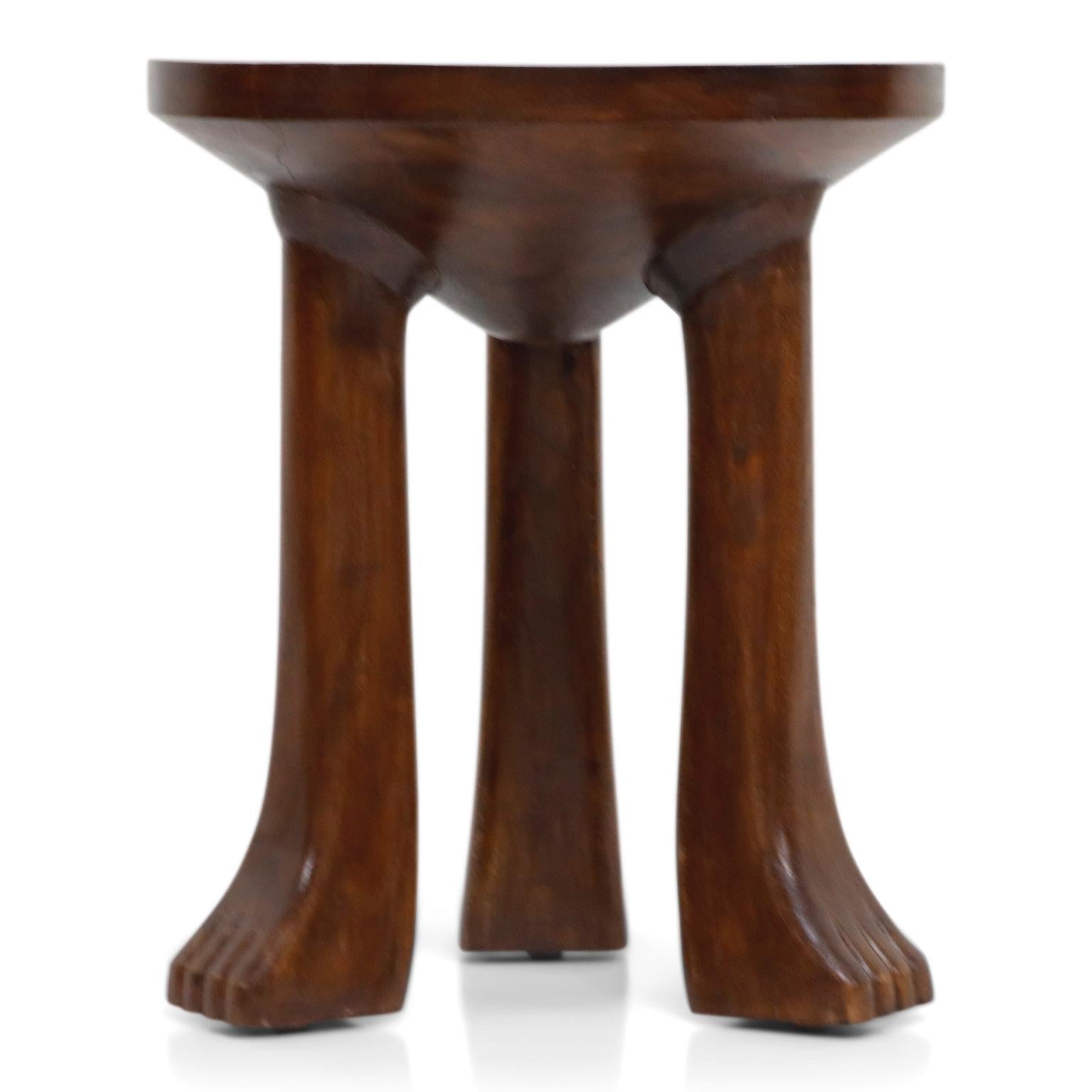 These attractive three legged carved teak stools (or side tables) are in the style of John Dickinson's 