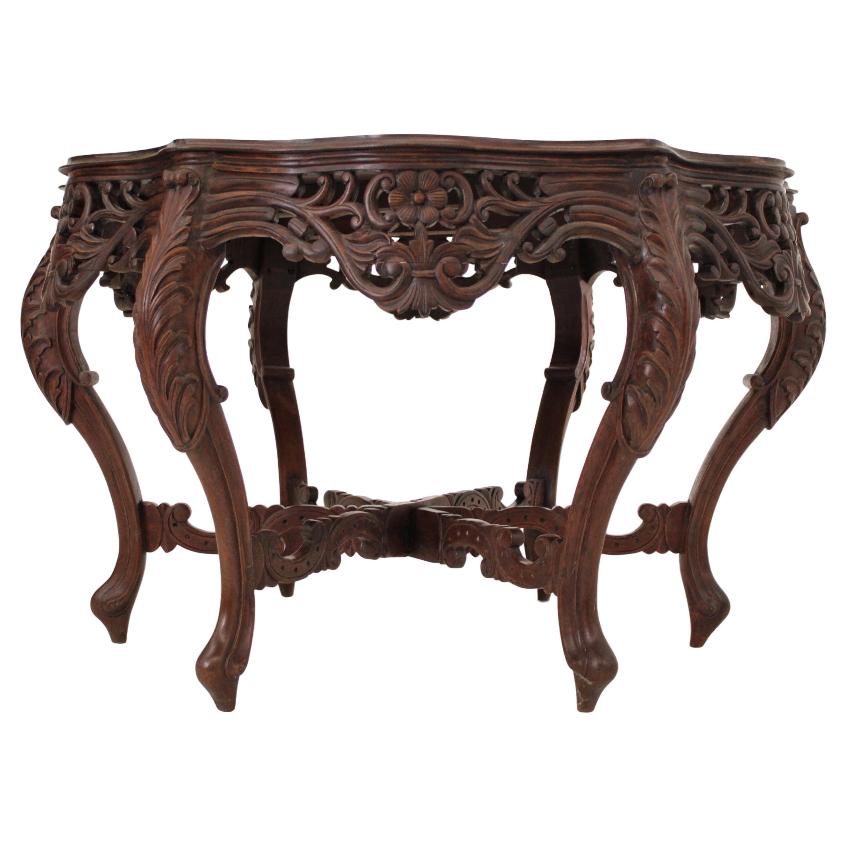 An exceptional carved Teak center table, with a serpentine-shaped top, carved from two broad planks of teak. The bombe-shaped sides add a touch of elegance. The table has the original set of intricately carved stretchers at the base and the