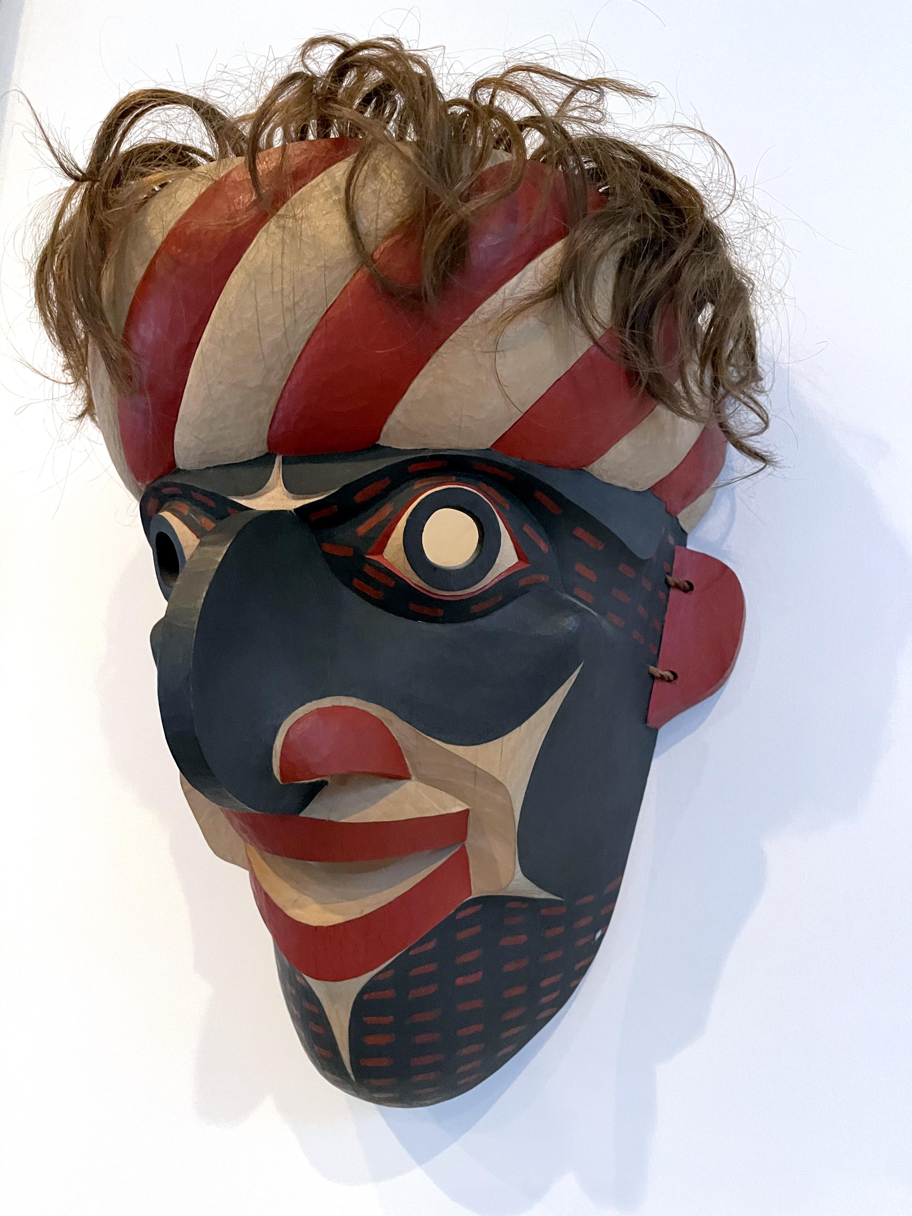 Un masque sculpté et peint dans la tradition des tribus amérindiennes de la côte nord-ouest du Pacifique, réalisé par David Frankel en 1994. Le masque a été sculpté dans du cèdre jaune et peint avec des couleurs rouges et noires contrastées selon un