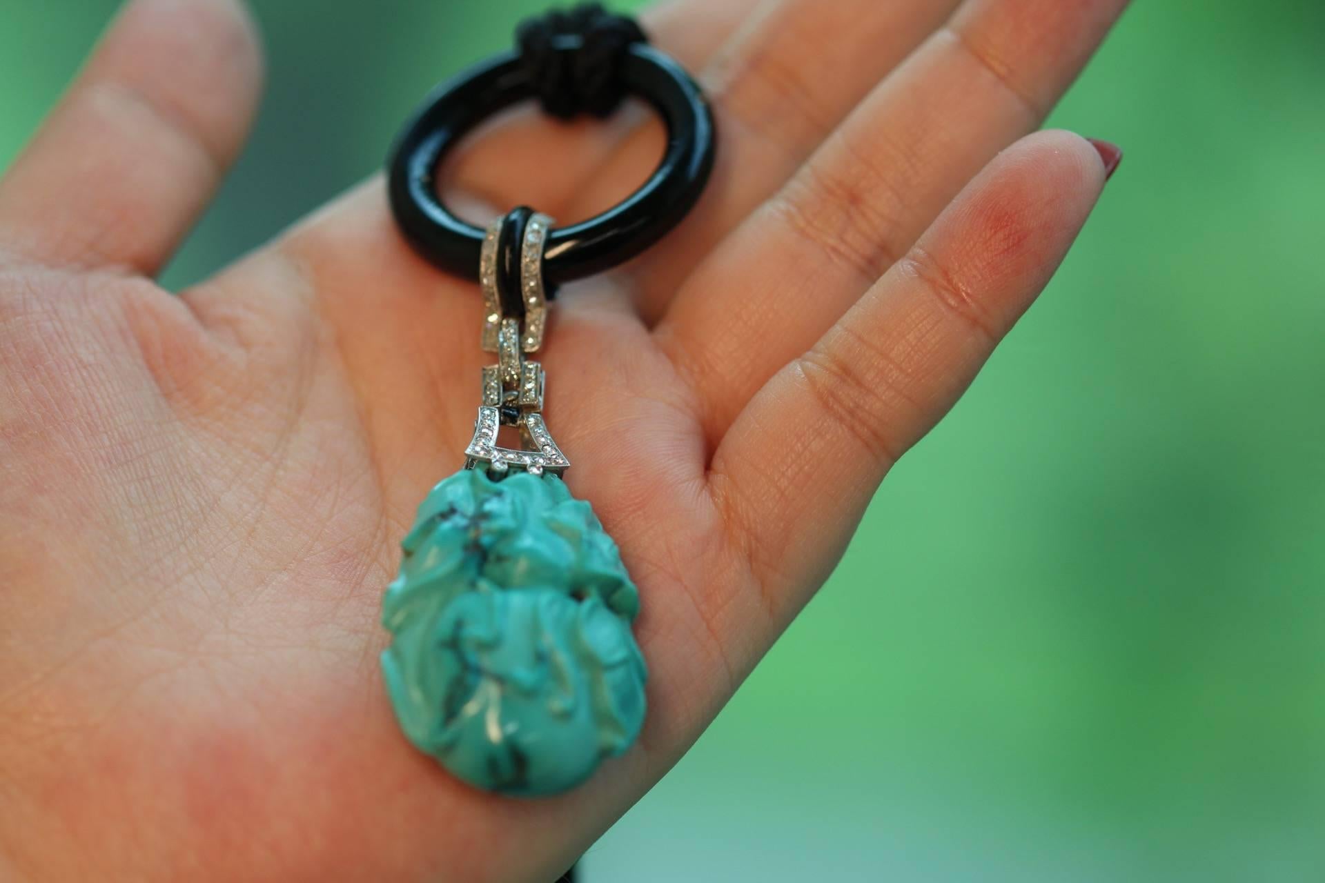 This gorgeous natural turquoise is carved to show a traditional Chinese motif of a fruit with leaves and flowers. It is attached at the top to a platinum and diamond design leading to an onyx circle. 

Chinese style and motifs were popular in the