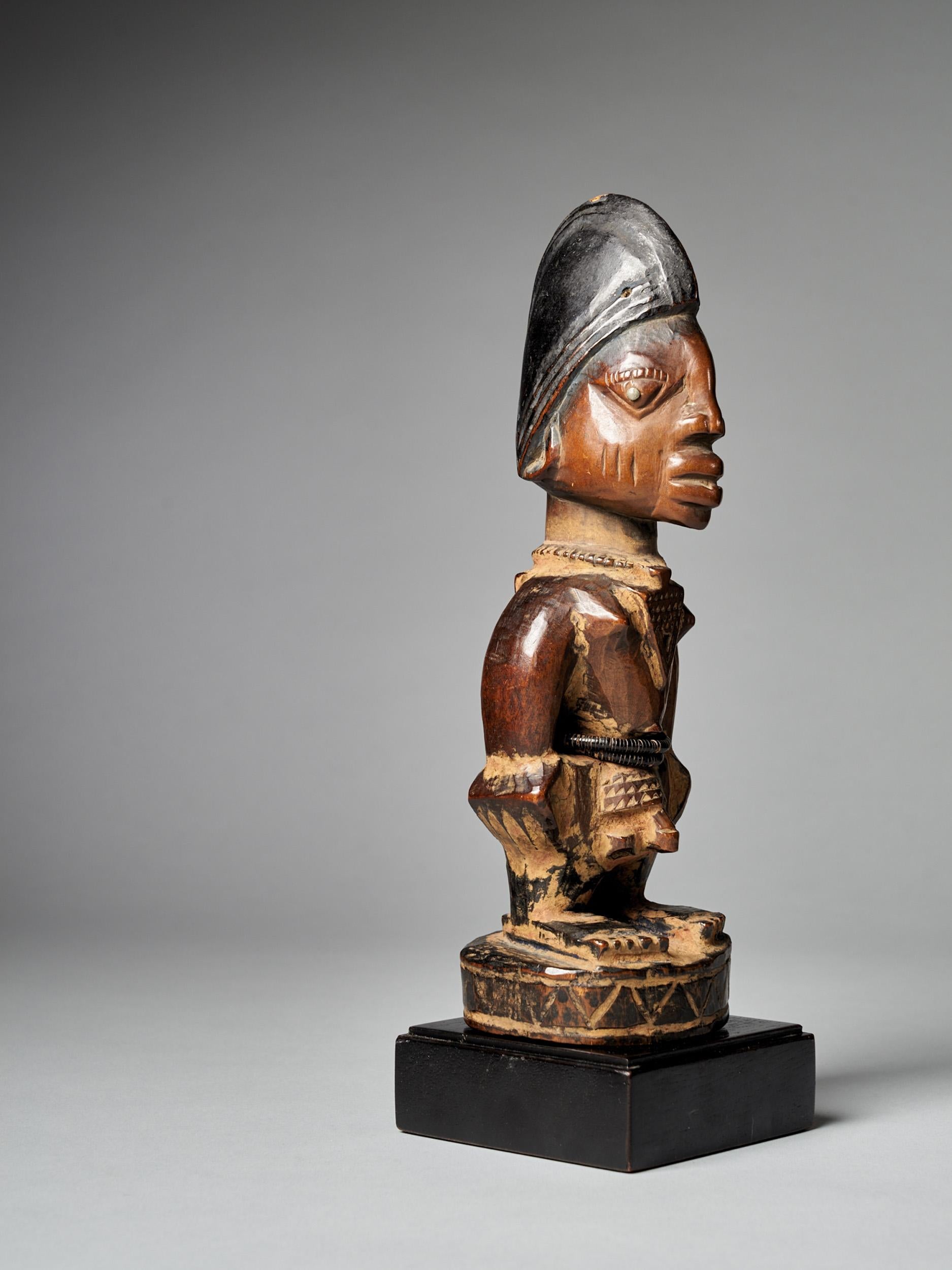 A finely carved significant Yoruba Male Ibeji figure with a tall headdress, expressive eyes, original bead belt and heavy wear and polish from native use. Areas of encrusted camwood powder between arms and around feet. Though the cause of the high