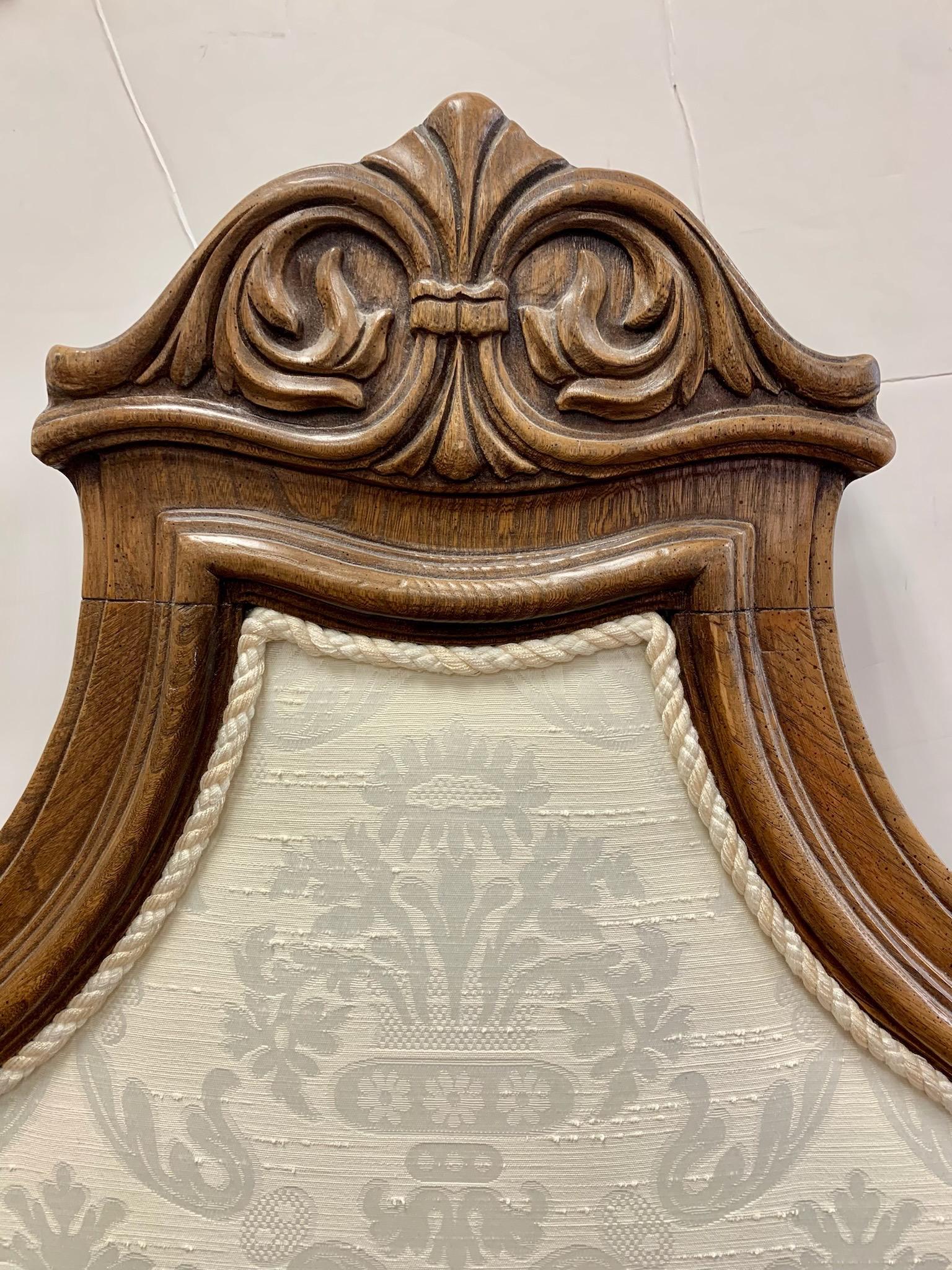 Vintage carved walnut framed king headboard upholstered in a neutral cream damask fabric with rope trim.