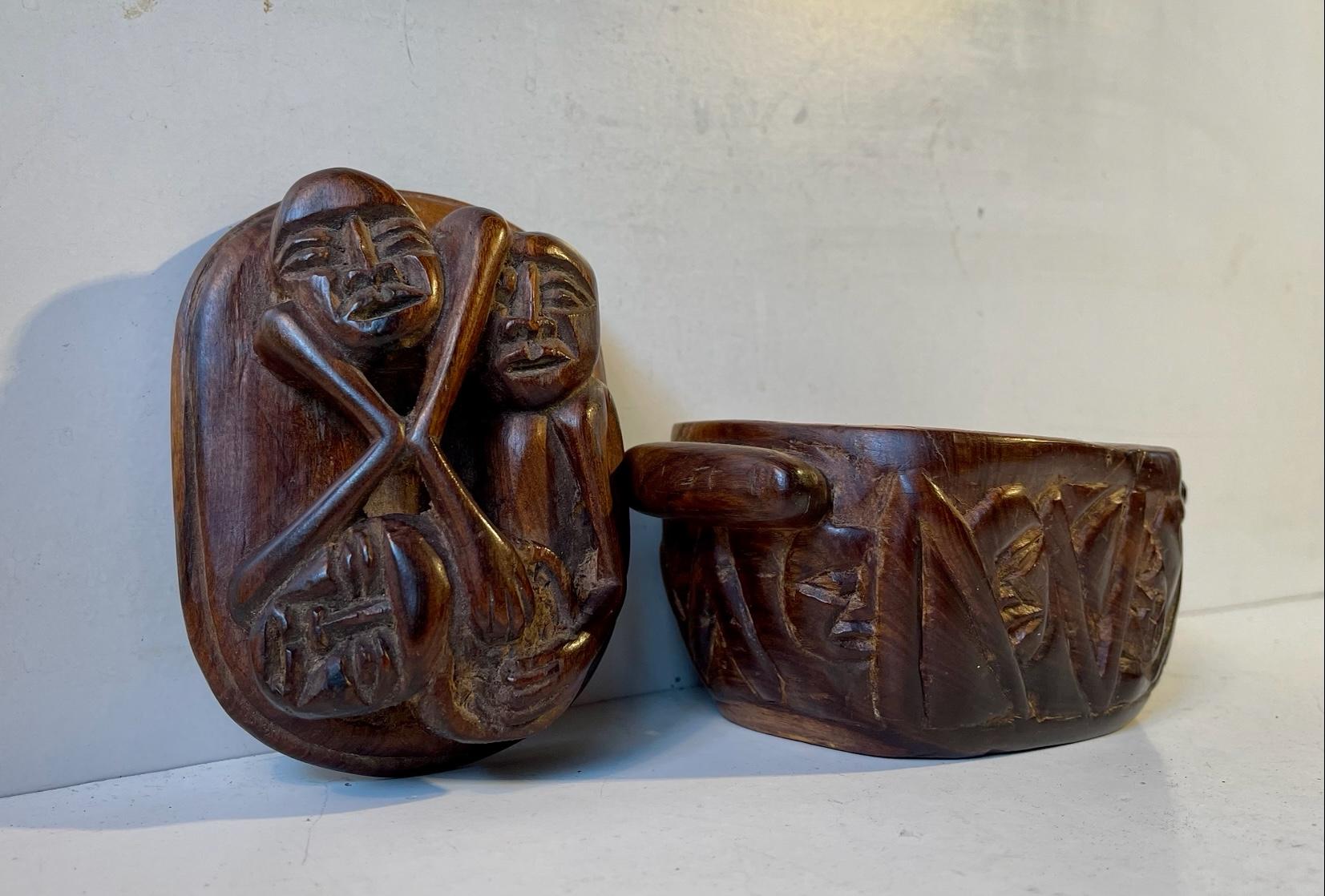 A hand carved wooden canister or jar with occult - ritualistic motifs. The lid/front depicts a couple of persons eatings the brain of a cross sected/half human head. The bottom part is aggressively cut in a geometric pattern and with alluring faces