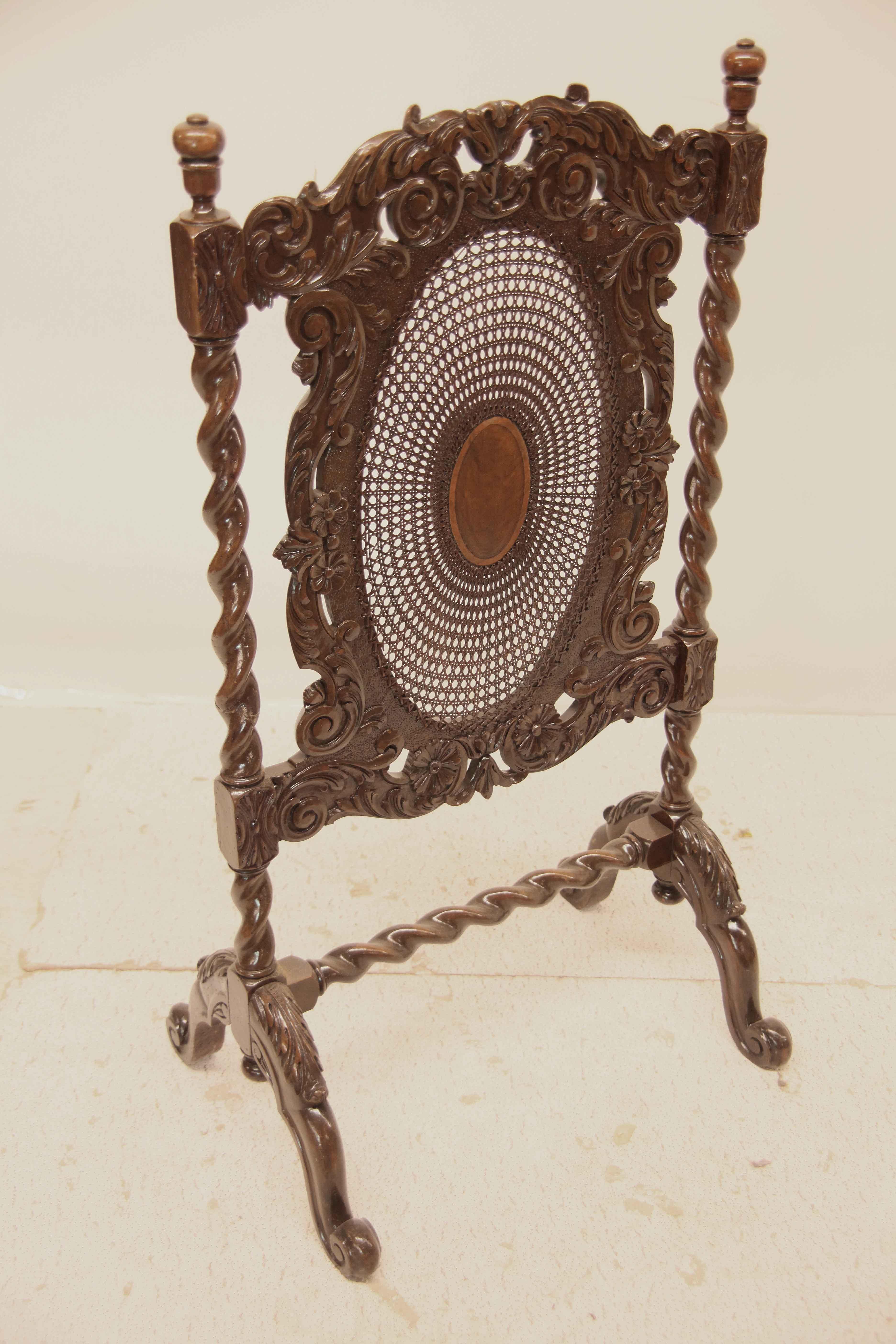 Carved walnut barley twist and cane firescreen, featuring arabesques, rosettes, and foliate carved in high relief, central walnut veneer oval medallion surrounded by cane, this is supported by barley twist stiles with turned finials. The lower